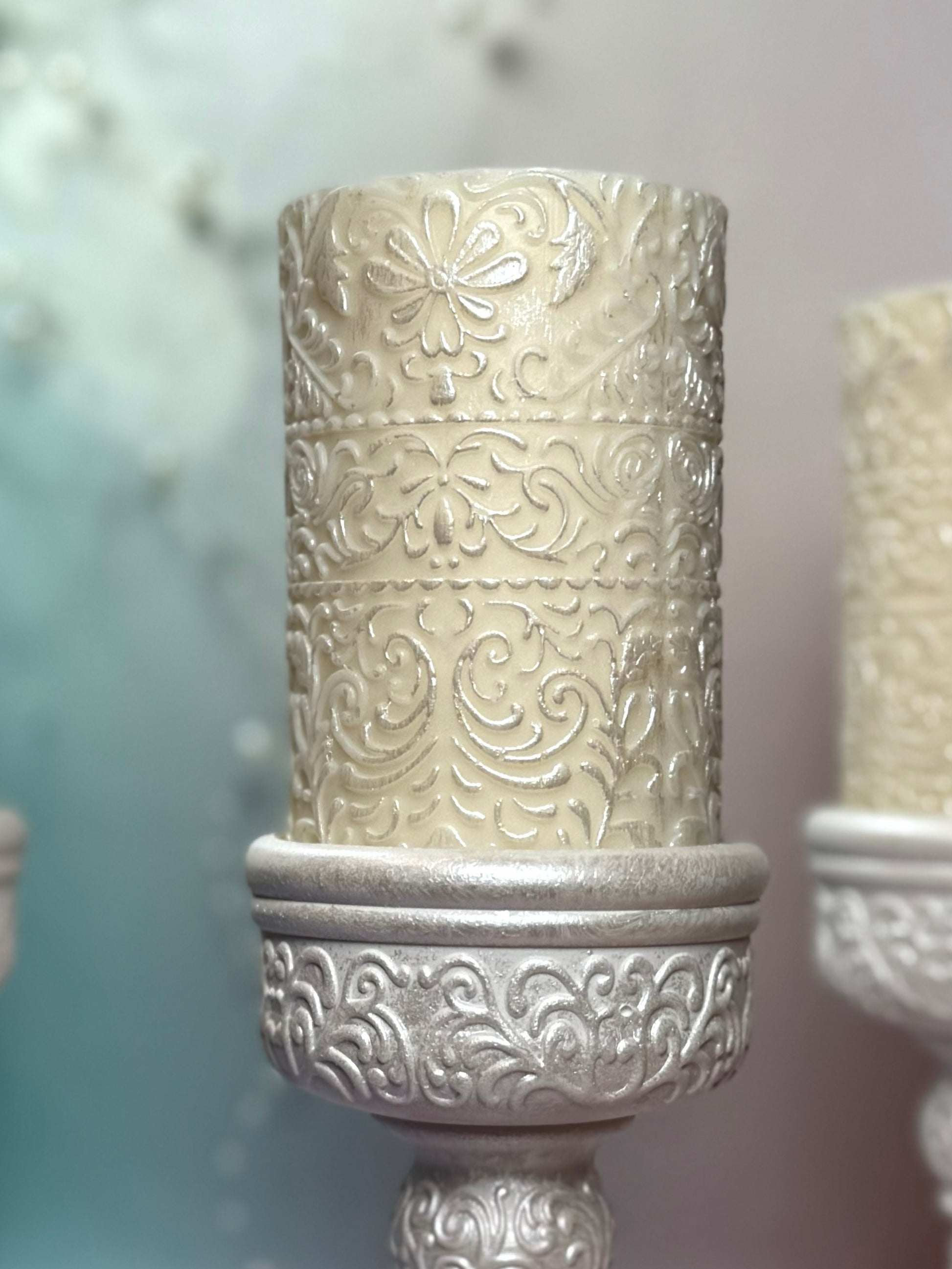 Macro detail of the embossed floral pattern on the soy wax pillar candle with shimmering pearl-white accents.