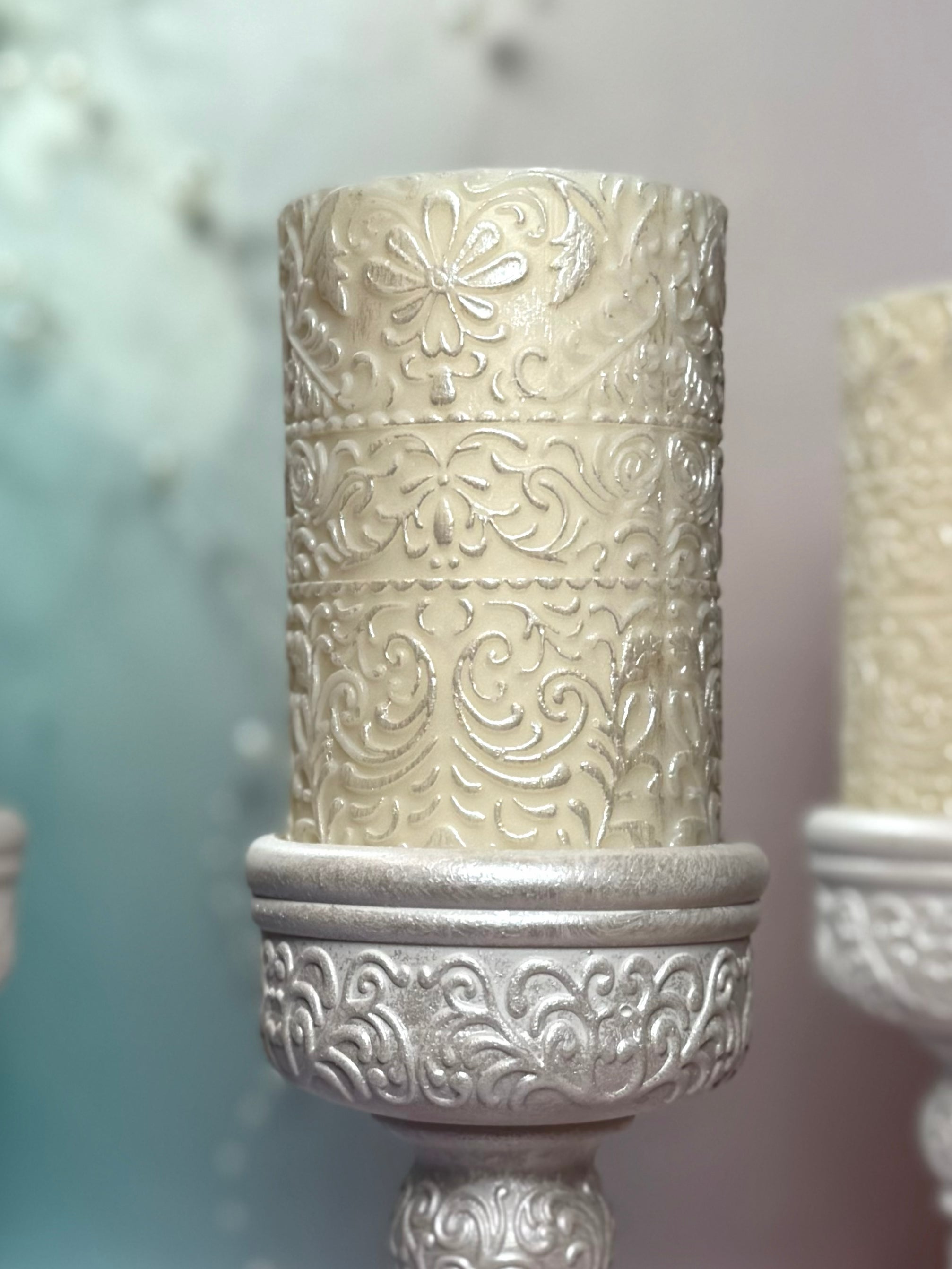 Macro detail of the embossed floral pattern on the soy wax pillar candle with shimmering pearl-white accents.