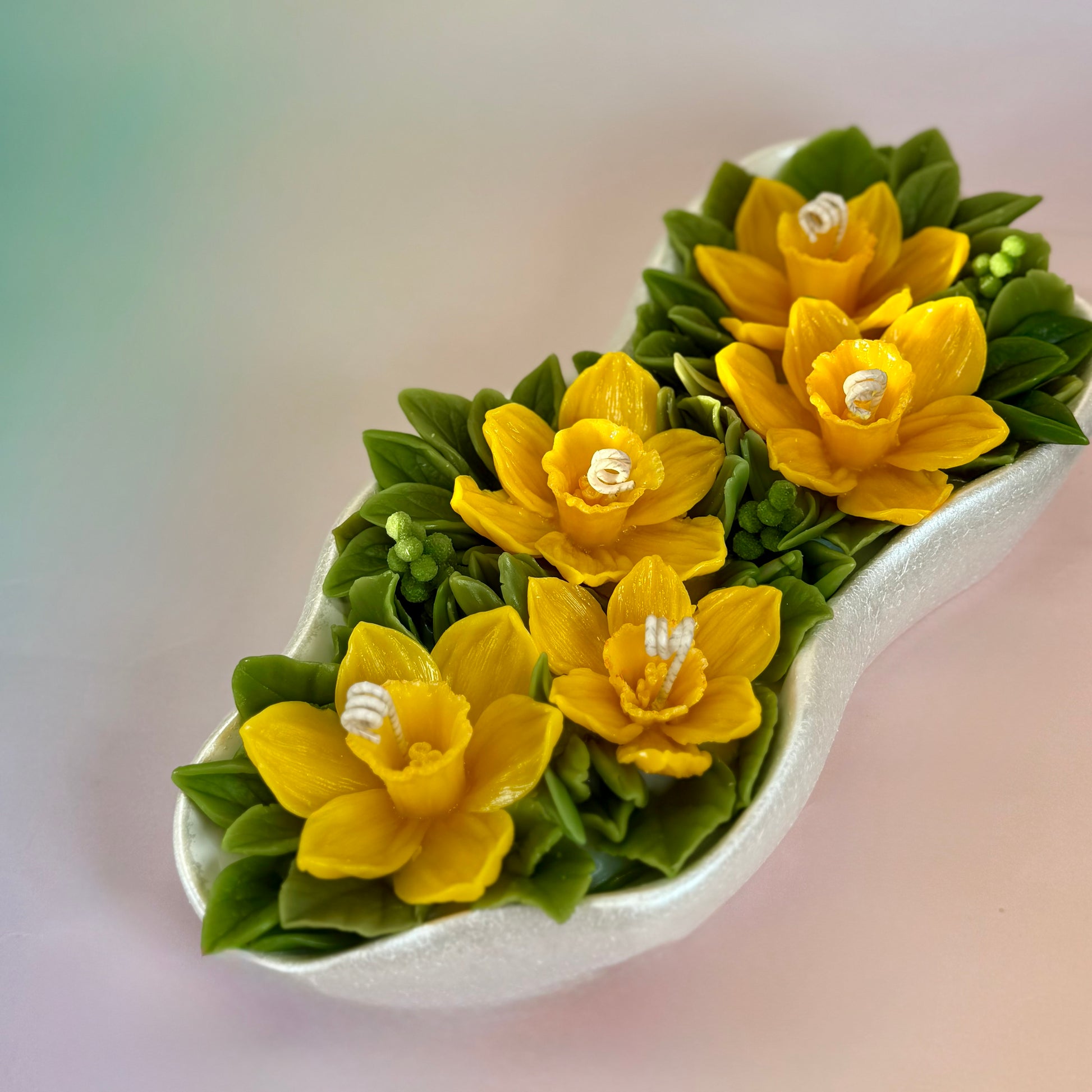 Angled top view of an ornate daffodil wax garden candle in a shimmering pearl-white Jesmonite boat tray.