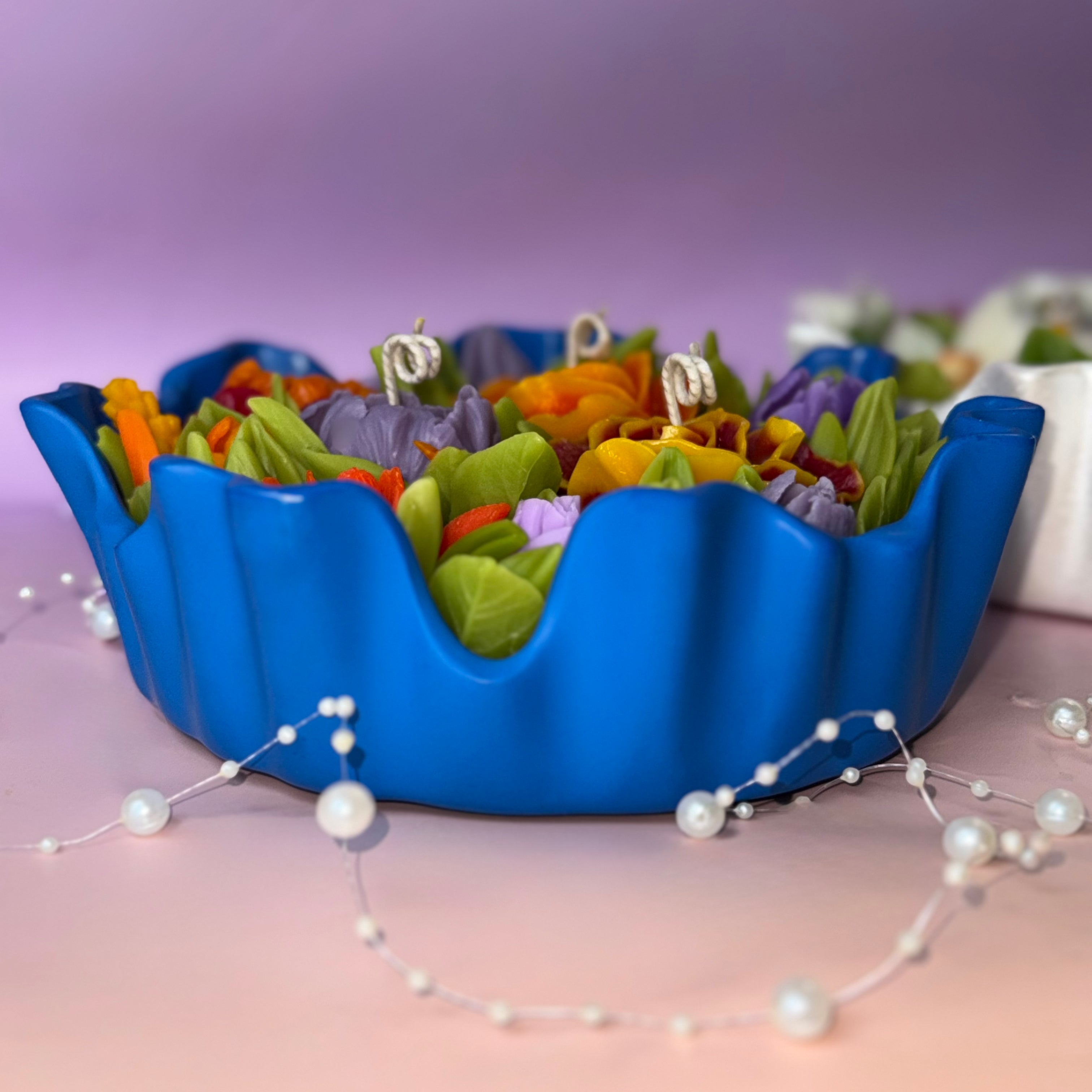 Profile view of the distinctive vibrant blue fluted bowl containing a lush, multi-wick floral centrepiece candle with a focus on the realistic wax foliage.