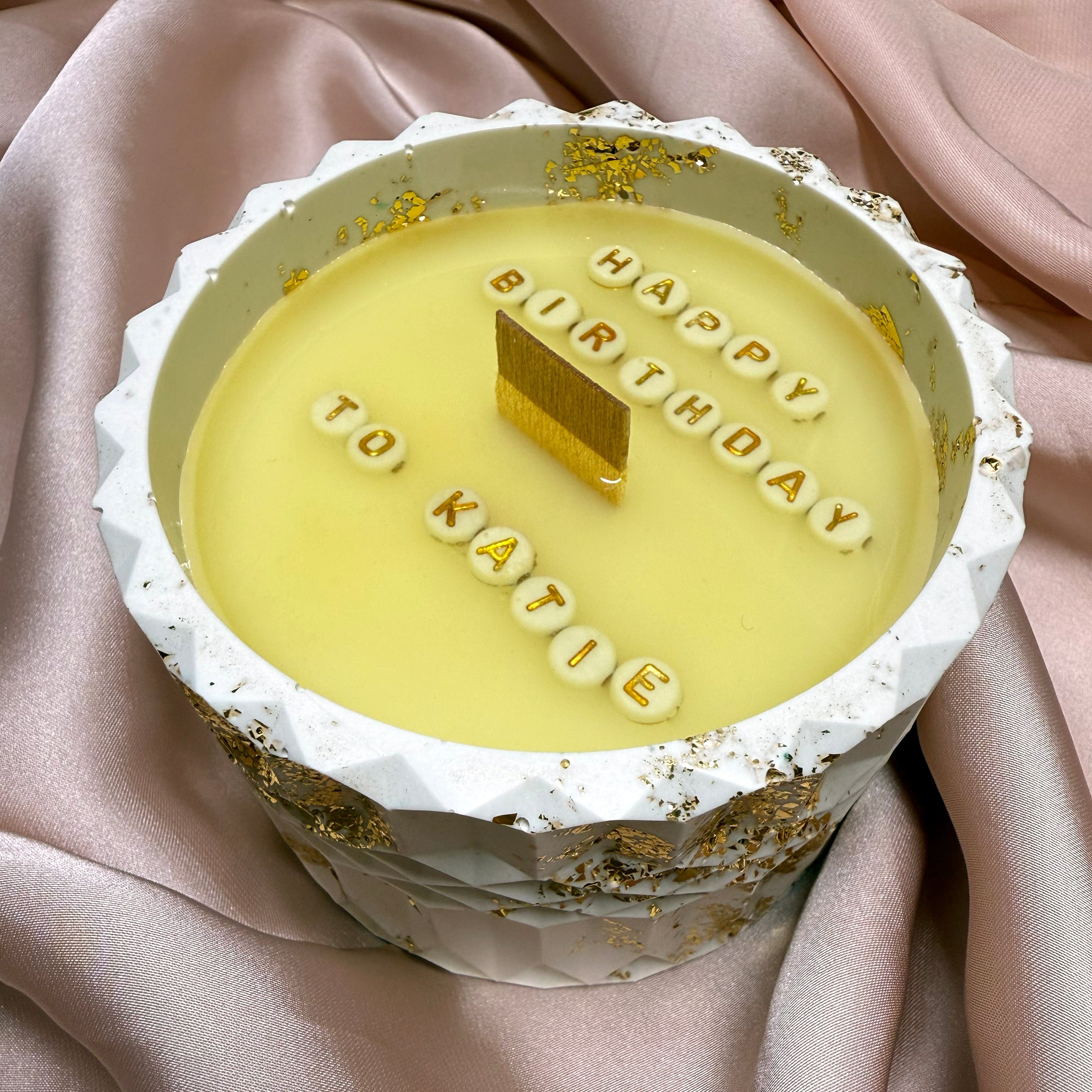 Personalised soy wax candle revealing a hidden 'Happy Birthday' message in a white Jesmonite pot with luxury gold leaf flakes.