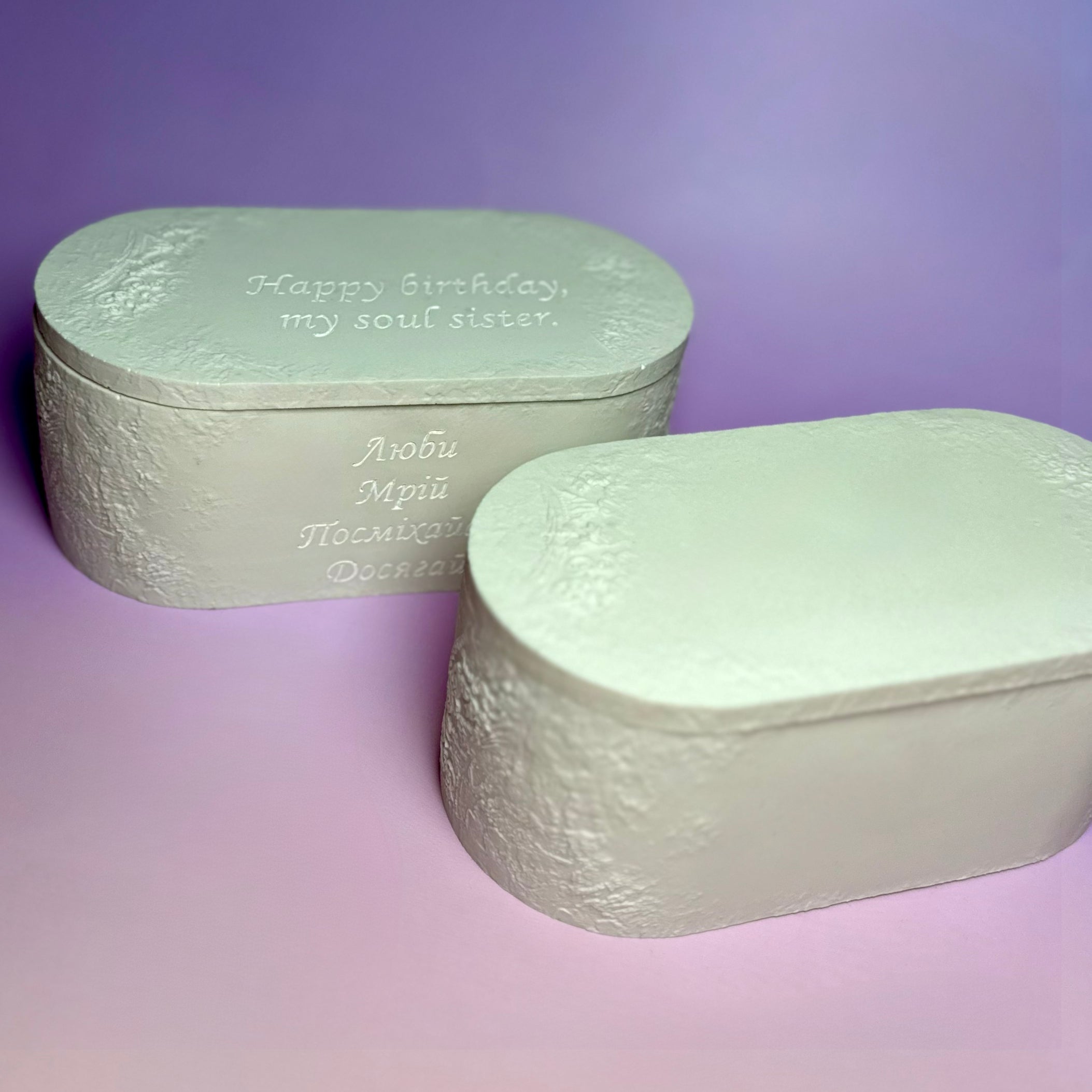 Two bespoke candles in white Jesmonite containers, showcasing different personalised engravings on the lids and sides.