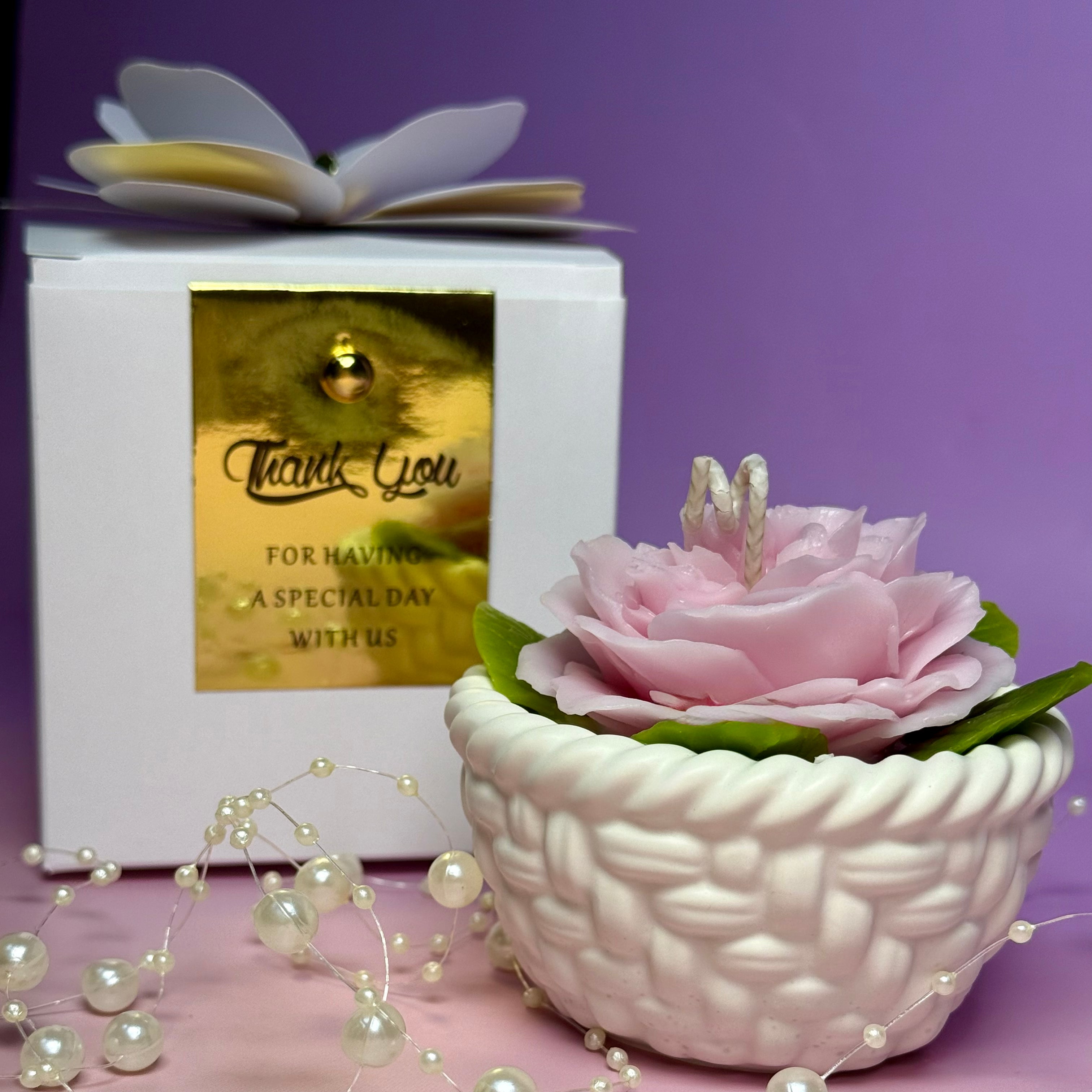 A handcrafted soft pink beeswax Abraham Darby rose candle nested in a white woven wax basket base, styled next to a white luxury gift box with a gold Thank You tag.