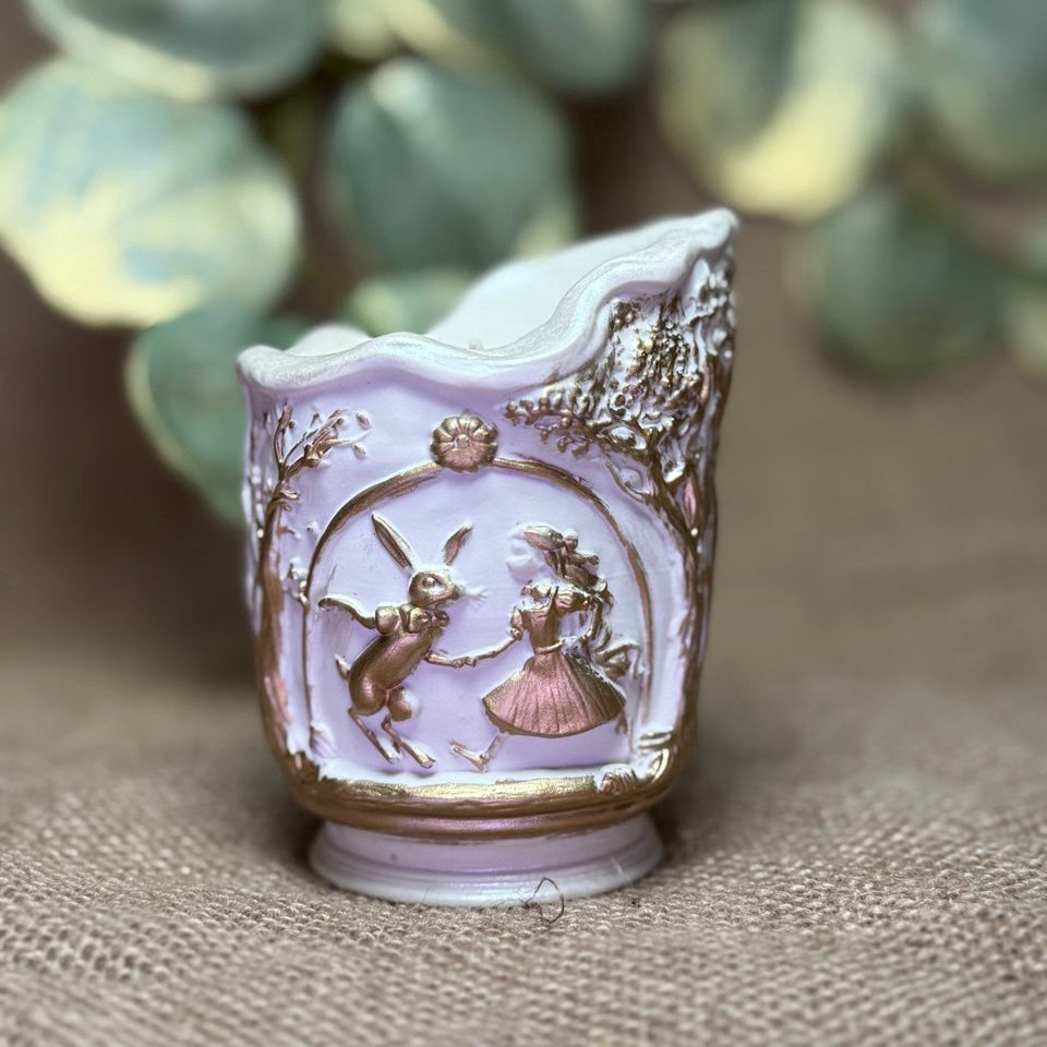 Front view of Alice in Wonderland hand-painted soy candle in a pearl-white Jesmonite holder, showcasing the high-relief scenic details of Alice and the White Rabbit in liquid gold