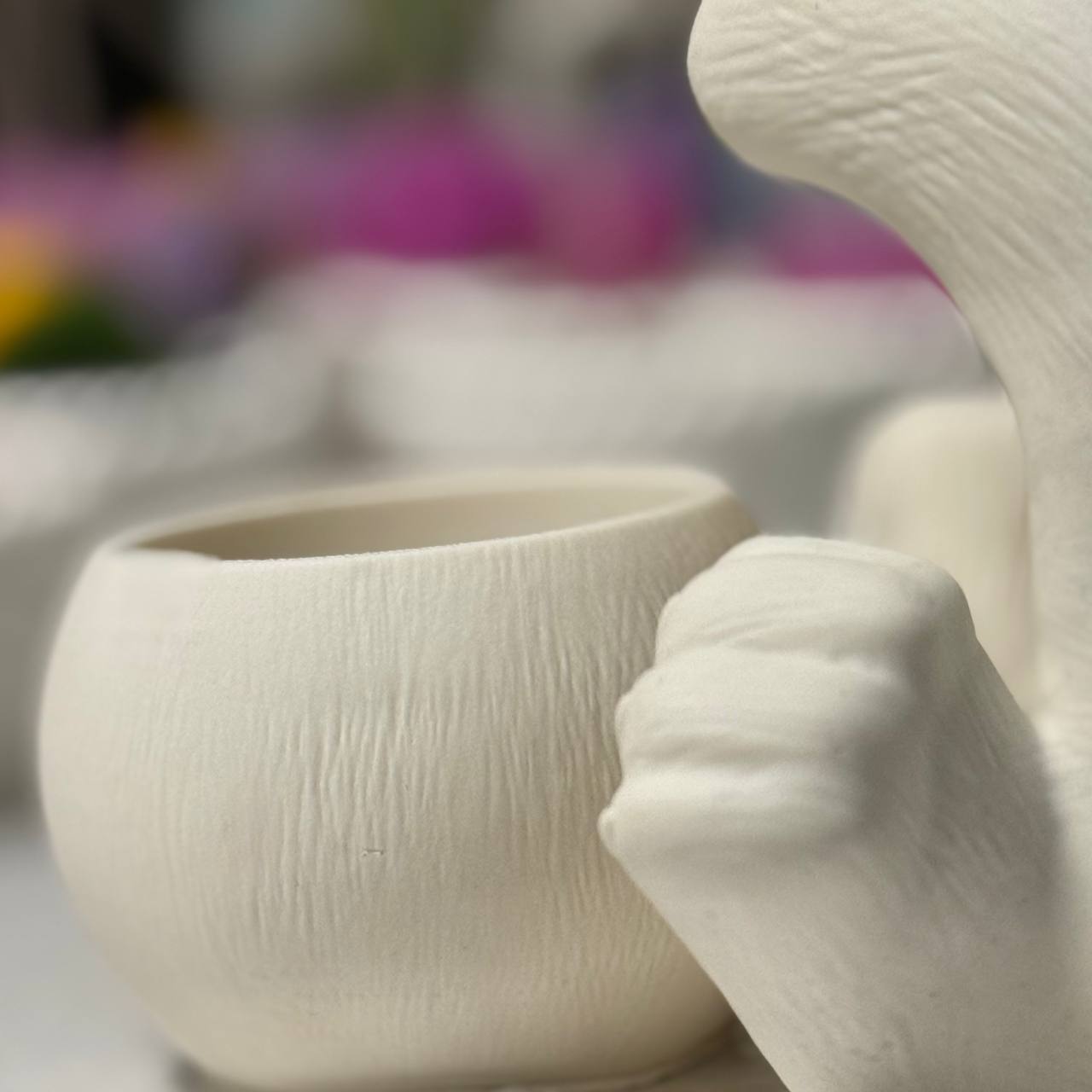 An extreme macro close-up of the integrated round Jesmonite candle vessel held by the hand-cast bunny character, illustrating the clean artisan pottery finish.