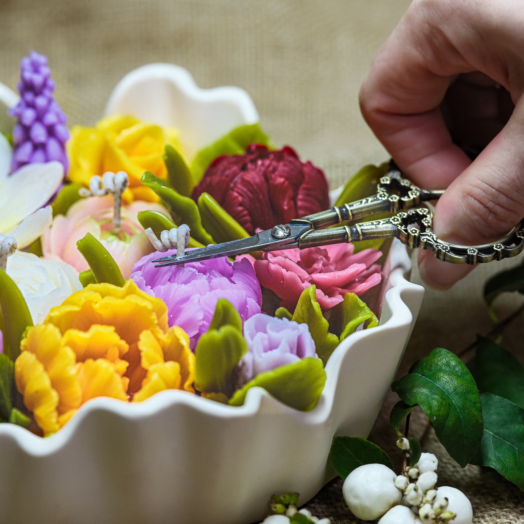 Artisan hand trimming the cotton wick of a detailed multi-coloured beeswax floral candle.