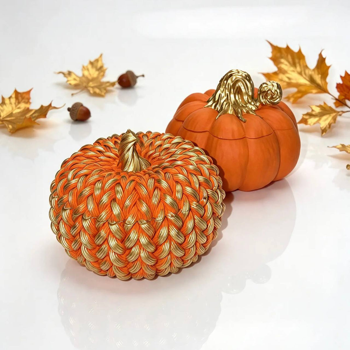 Handcrafted orange pumpkin candle vessels with gold stems displayed with autumn leaves and acorns