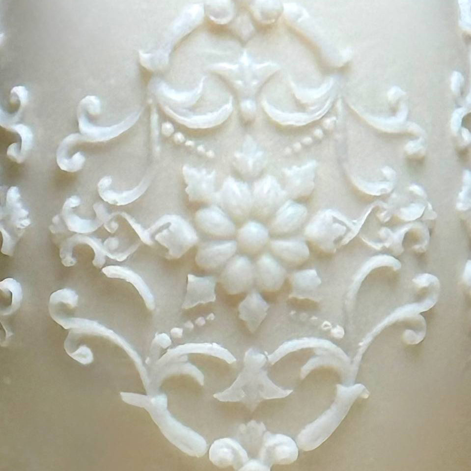 Close up macro shot of the high relief carved ivory style filigree and vintage patterns on a white handmade Easter egg candle.