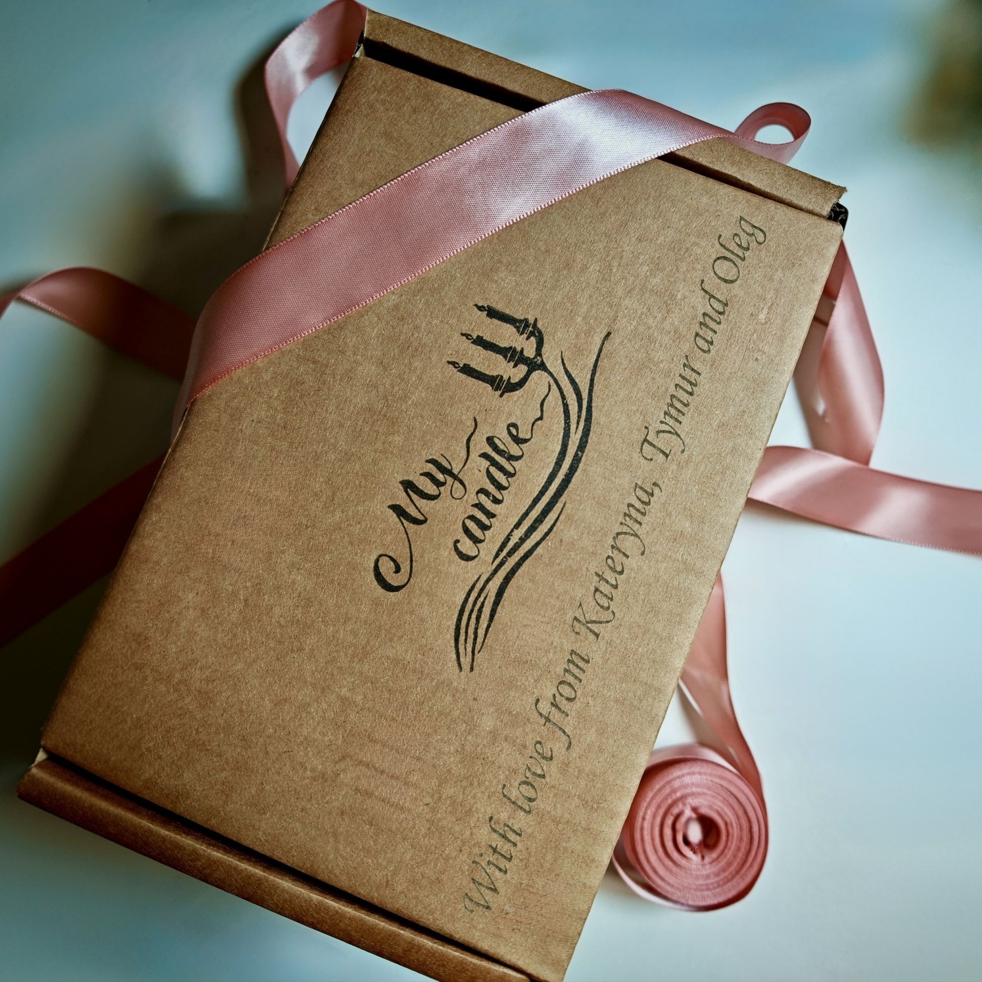 Close-up of a sustainable cardboard gift box featuring custom laser-engraved message "With love from friends" and an elegant pink satin ribbon.