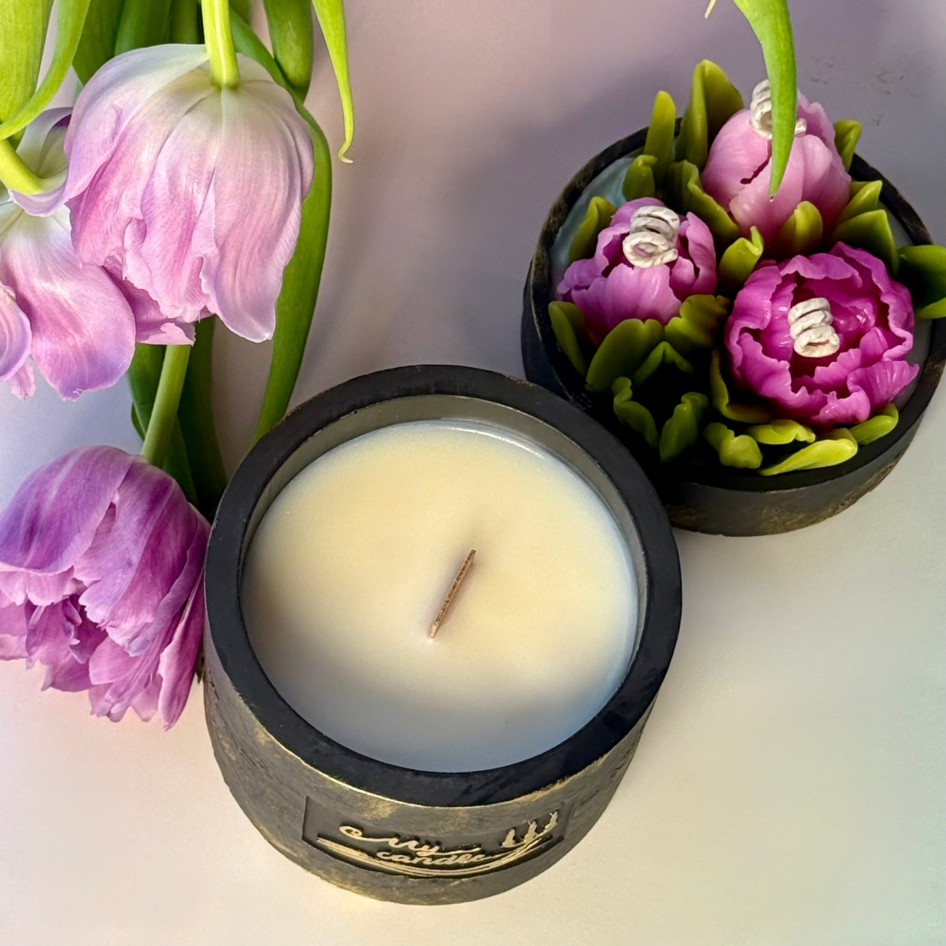 Luxury refillable soy candle UK with wooden wick in a black and gold Jesmonite vessel, shown from above next to a flower lid featuring purple beeswax tulips.