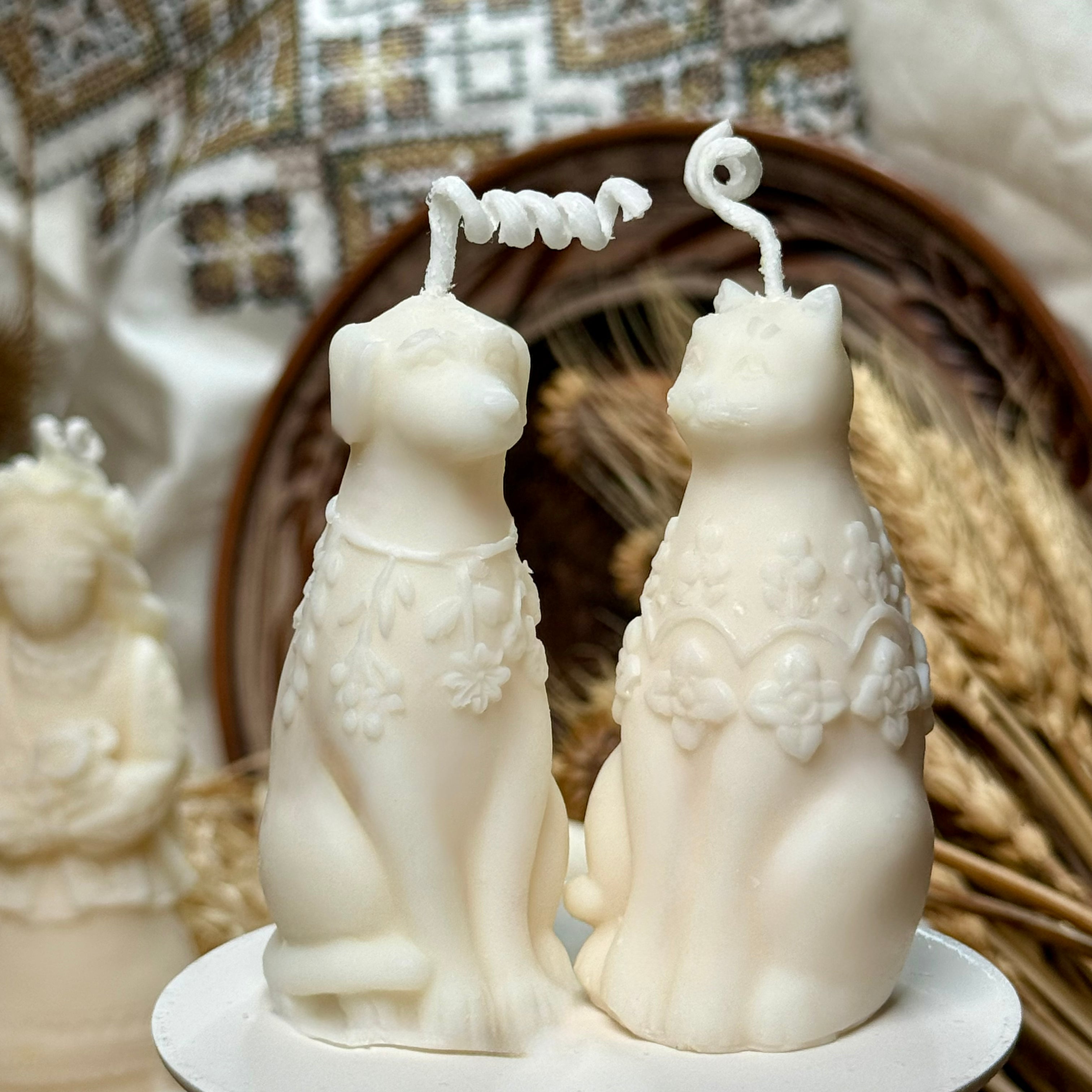 A close-up shot of the botanical dog and cat shaped soy wax candles in matte ivory, highlighting the intricate raised floral relief details on their chests and their playful curled wicks.