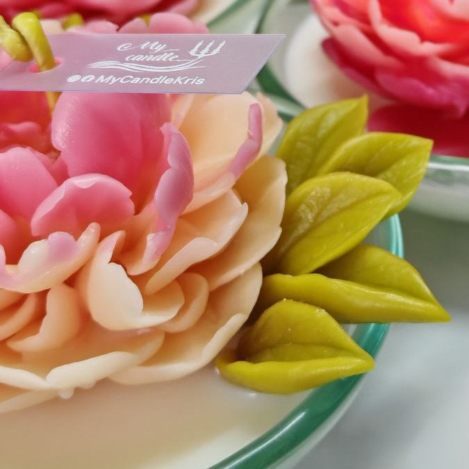Close-up of delicate green beeswax leaves and pink peony petals on a soy wax base.