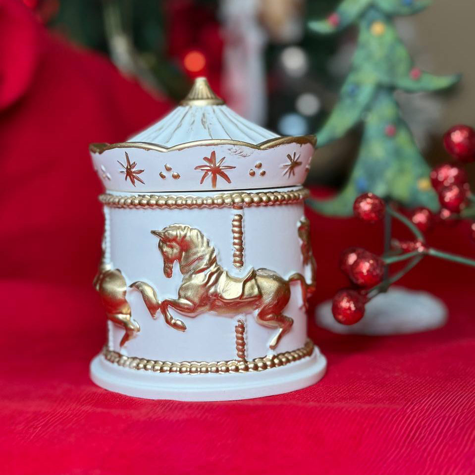 Handmade white and gold carousel horse scented candle in a Jesmonite pot against a festive red background, premium UK luxury home décor gift.