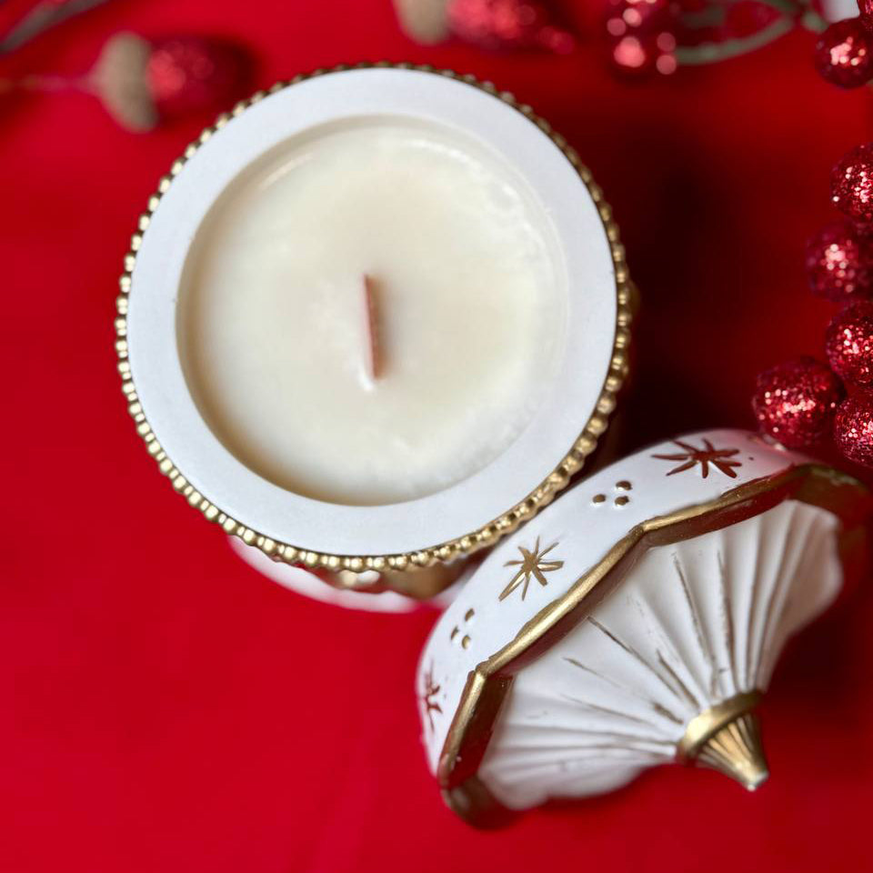 Top view of a handmade carousel horse scented candle in a white and gold Jesmonite pot with a wooden wick, set against a festive red background, premium UK luxury home décor gift.