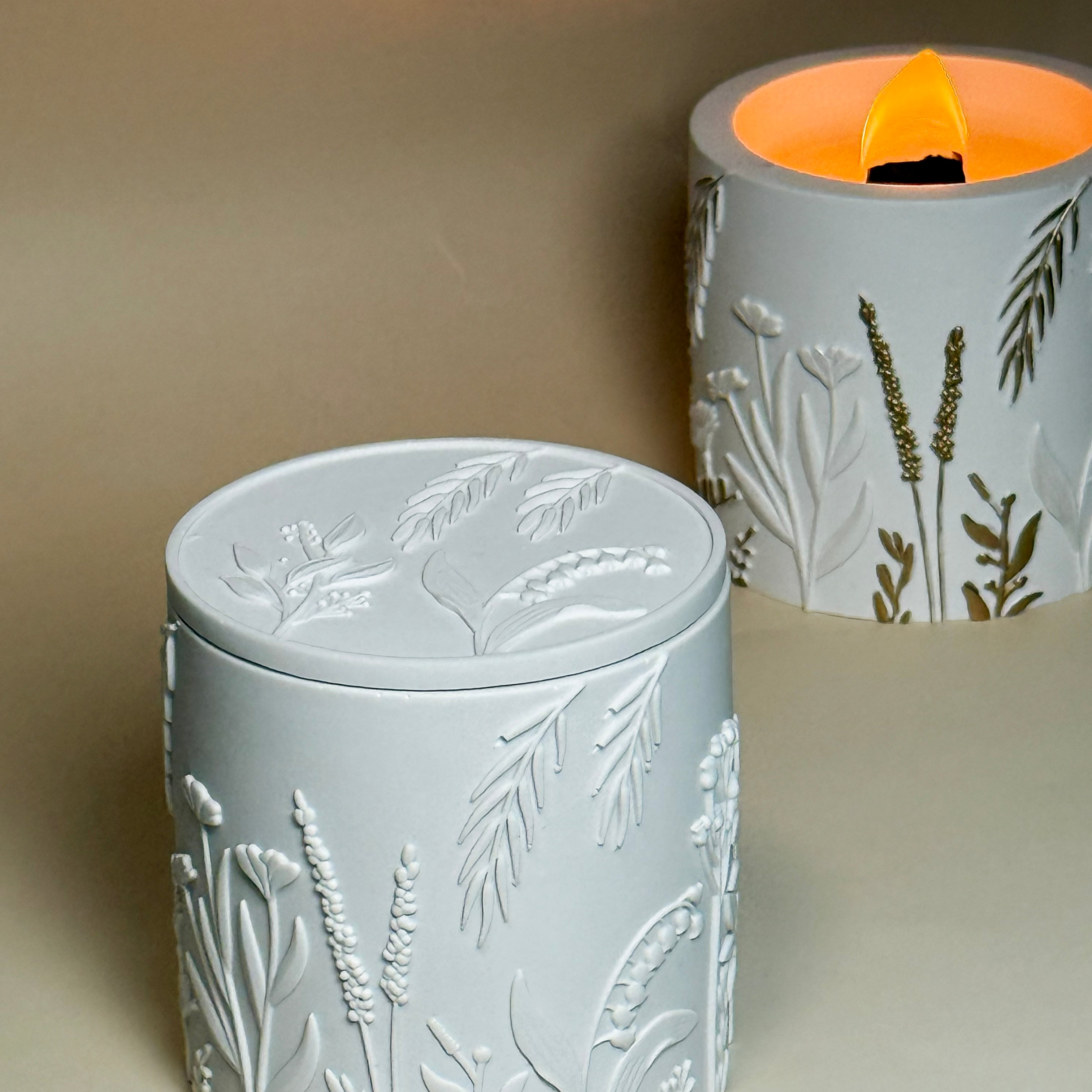 A closed classic white botanical relief candle jar made from Jesmonite, showcasing the clean architectural wildflower patterns on the vessel and its matching lid.