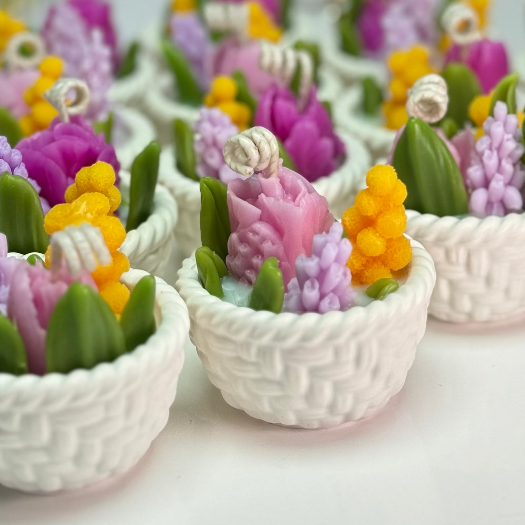 A detailed close-up shot focusing on the intricate woven pattern of the white Jesmonite baskets and the curled cotton wicks arising from hand-sculpted beeswax flower petals.