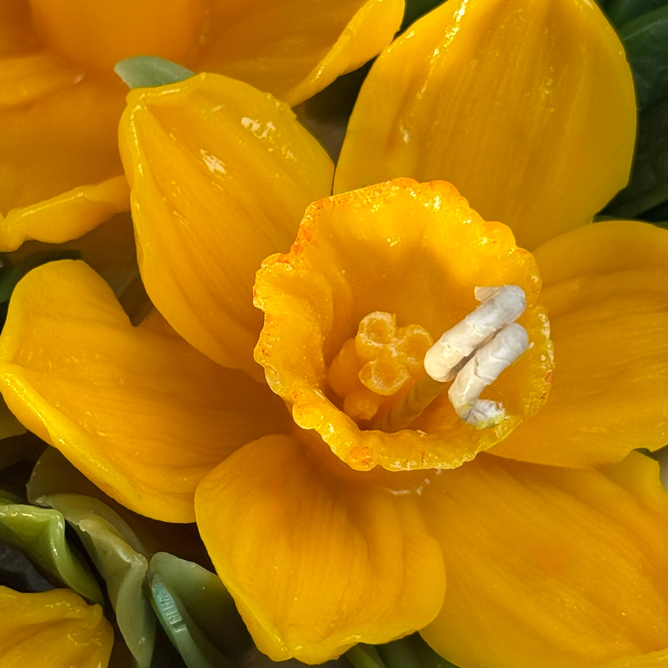 Extreme close-up of a hand-moulded beeswax daffodil showing realistic texture and yellow detail.