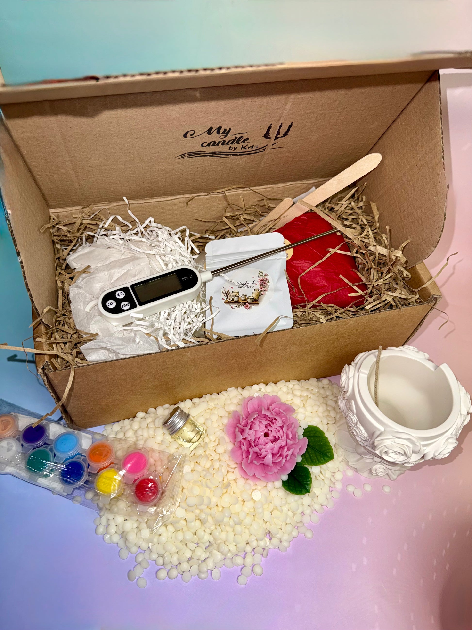 An opened kraft DIY candle making kit box branded with My Candle by Kris, showcasing a digital thermometer, soy wax pellets, paint pods, a pink beeswax peony, and an unpainted flower bouquet vessel.