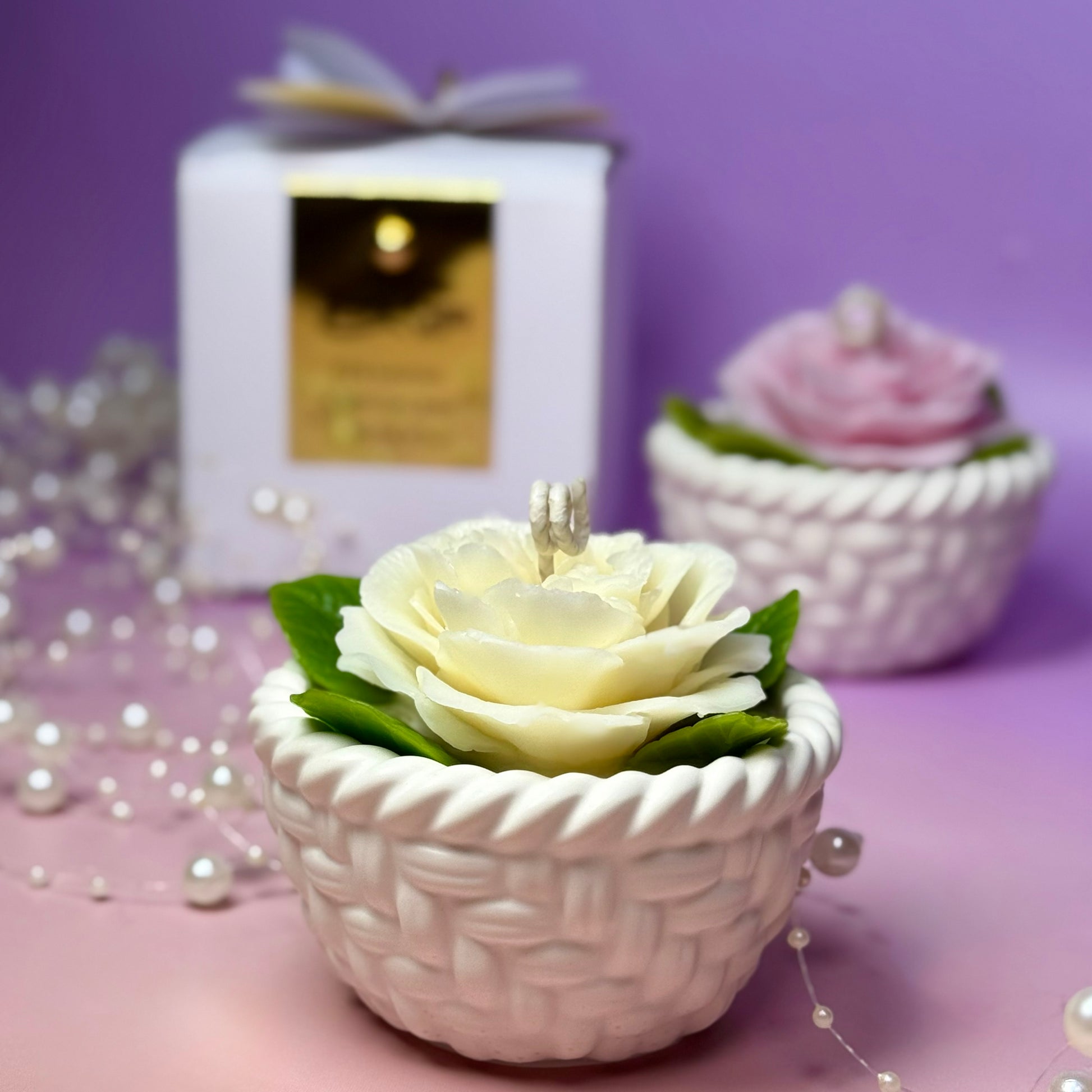 A focus shot on the ivory white version of the 80mm woven basket rose candle, infused with Fresh Morning Rose fragrance, styled with decorative white pearl strands.