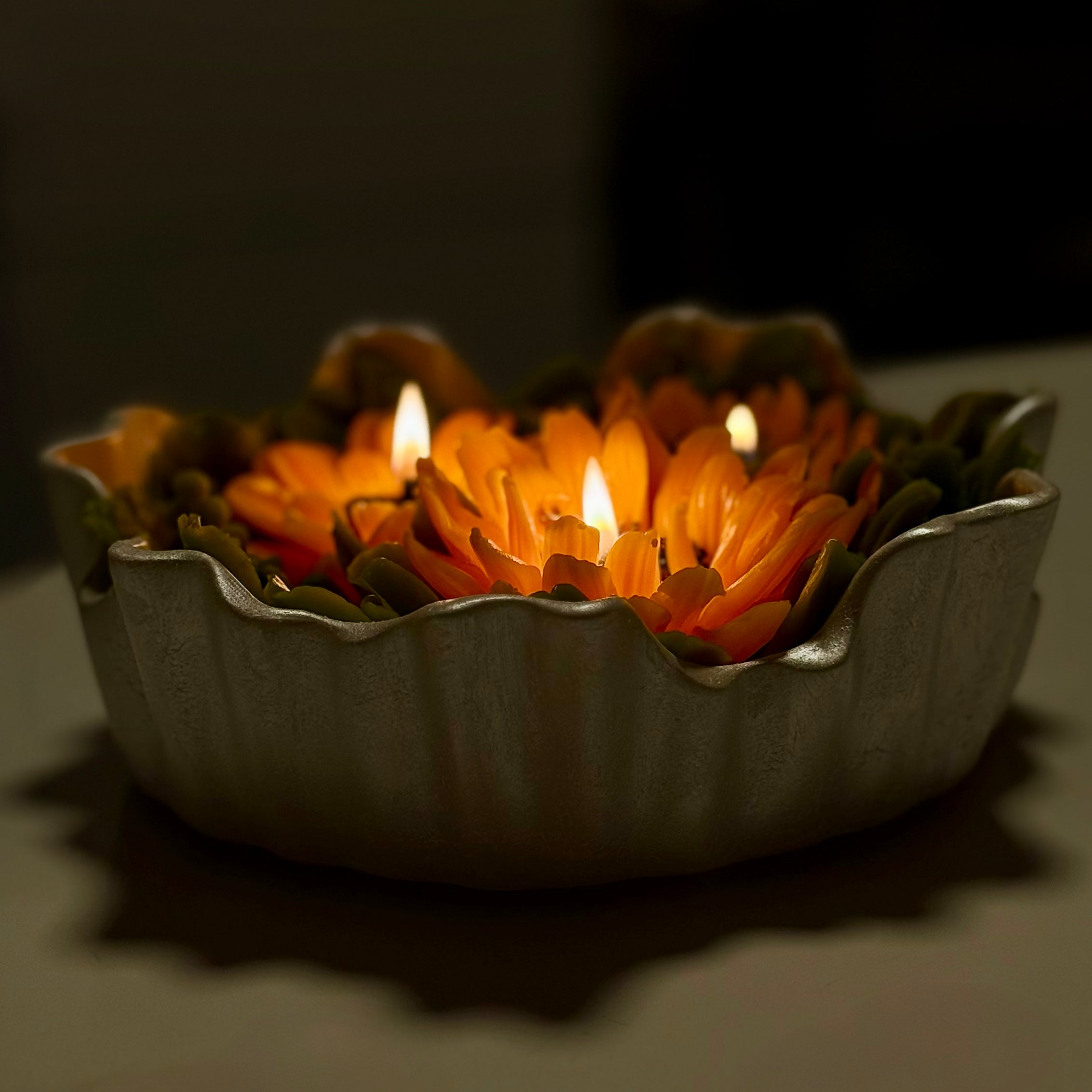 Side view of a grand sunflower bouquet candle lit in a dark room, highlighting the elegant fluted edges of the handcrafted pearl white Jesmonite bowl.