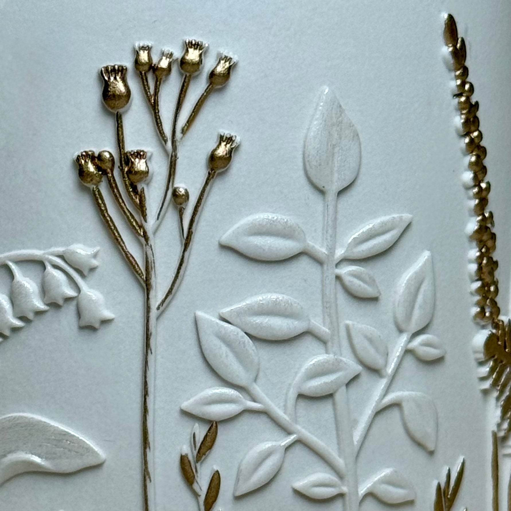 Detailed close up view of the hand-painted gold highlights on the botanical wildflower relief pattern of a premium Jesmonite candle container lid.