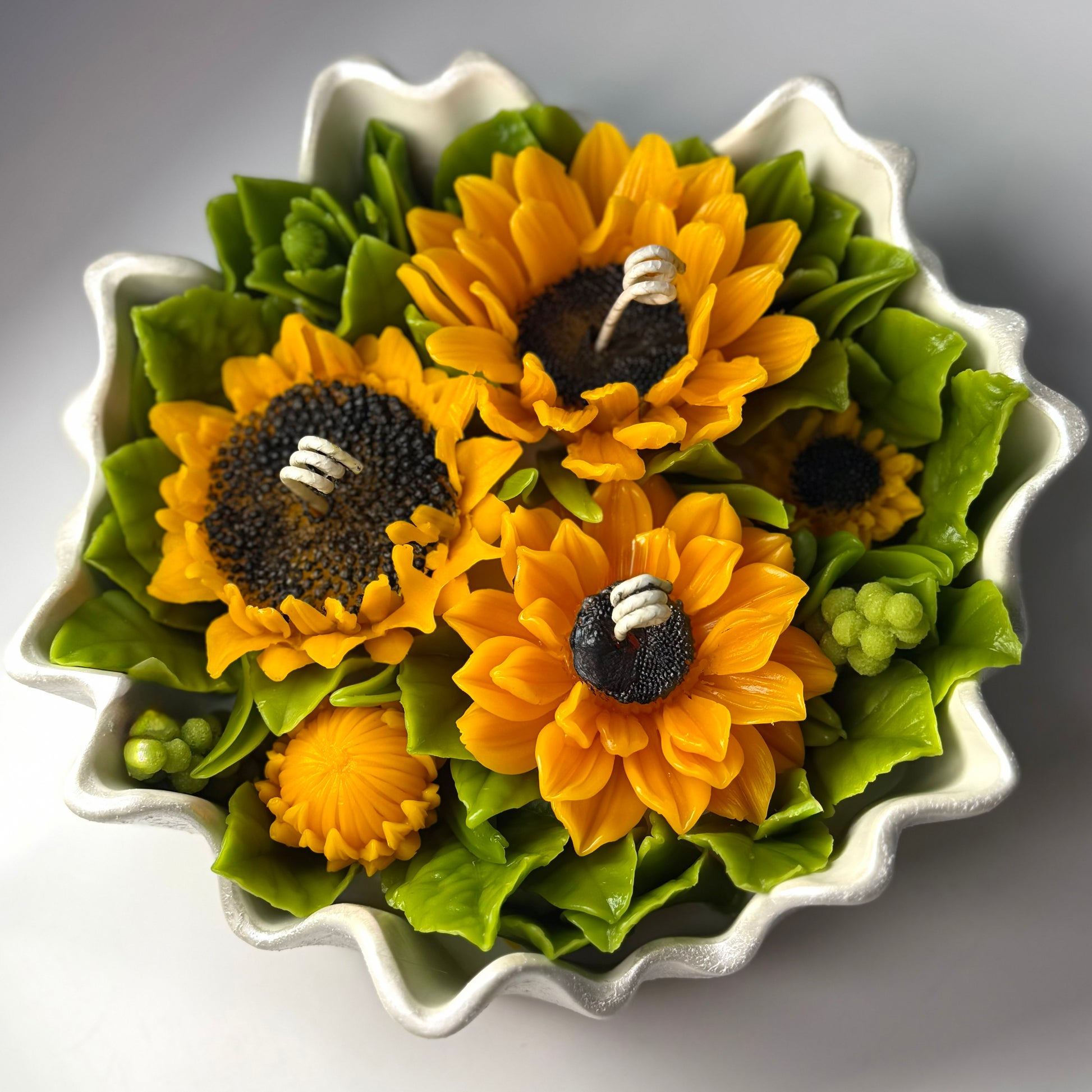 Close-up side perspective of the 20cm scalloped Jesmonite bowl hand-painted with a shimmering pearl white glaze, filled with vibrant sunflower wax sculptures.