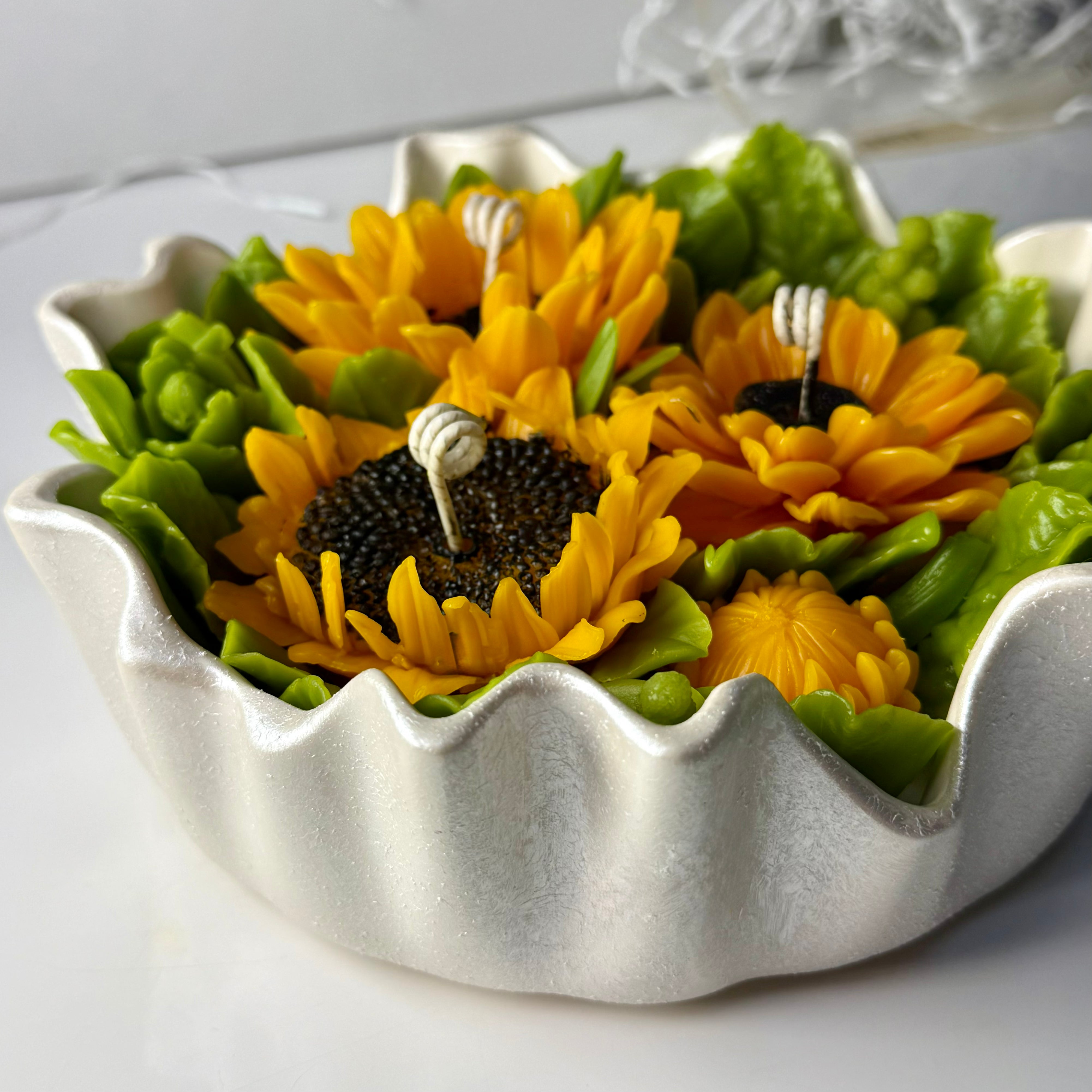 Close-up side perspective of the 20cm scalloped Jesmonite bowl hand-painted with a shimmering pearl white glaze, filled with vibrant sunflower wax sculptures.
