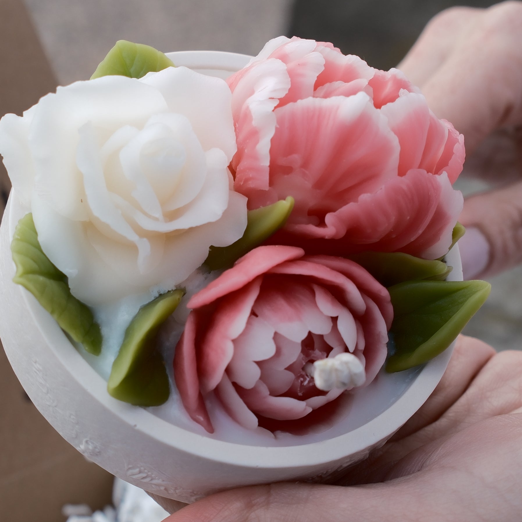 Detailed close-up of pink and white handcrafted beeswax flowers (rose and ranunculus) on the decorative lid.