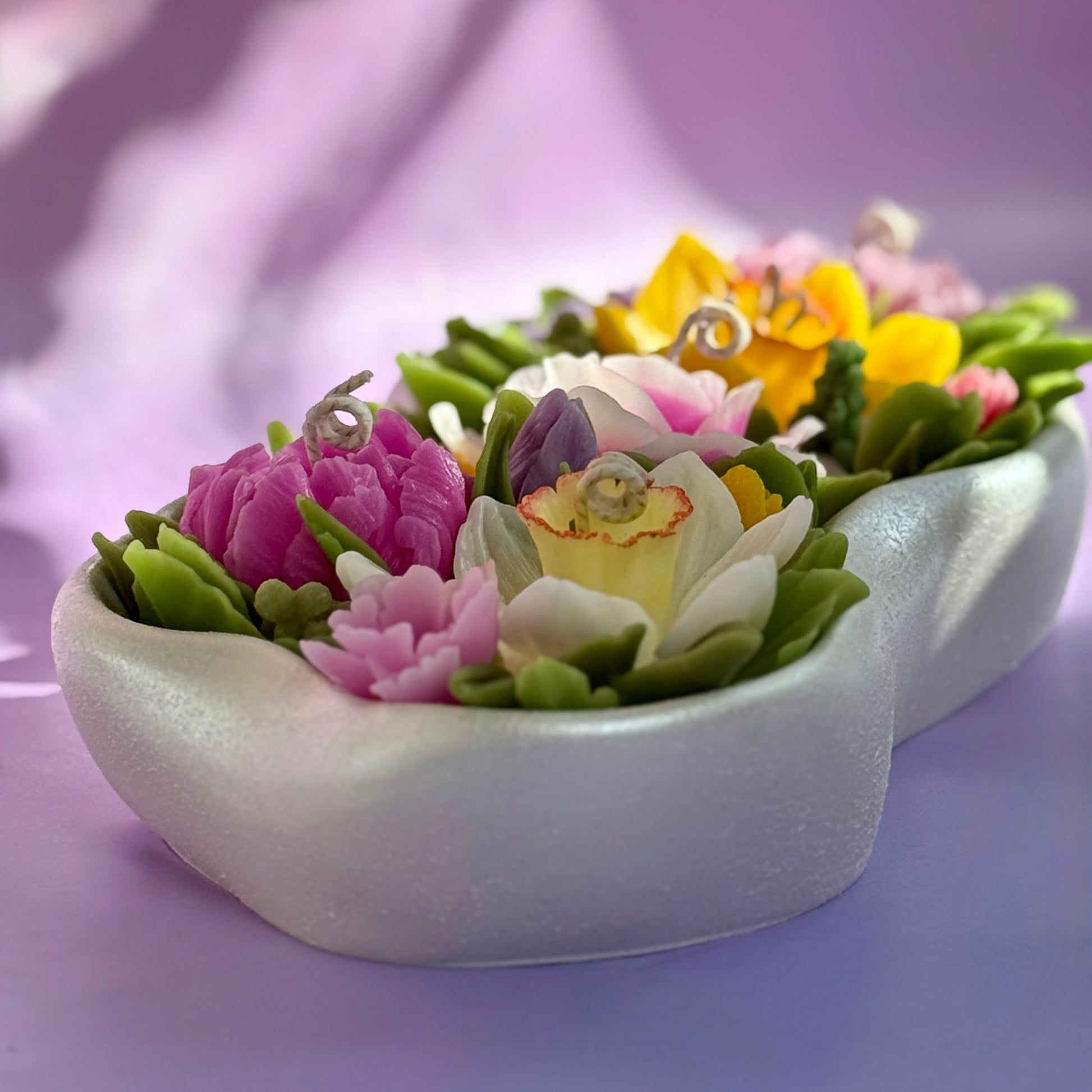 Close up of an intricate pink beeswax rose and botanical greenery on a soy wax base.