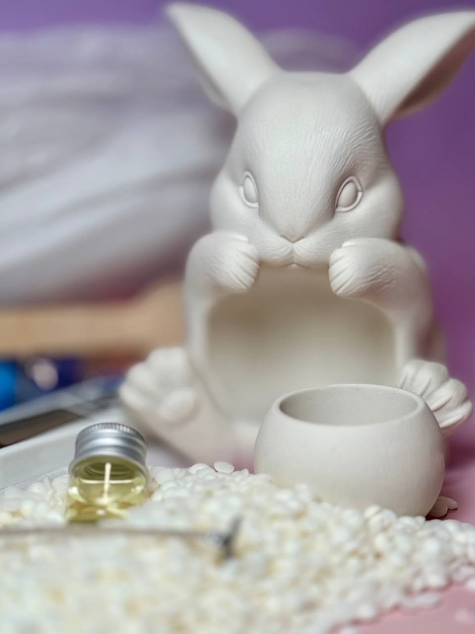 An unpainted Jesmonite bunny candle holder vessel next to a premium candle fragrance oil bottle and soy wax flakes, part of an eco friendly craft kit made in the UK.