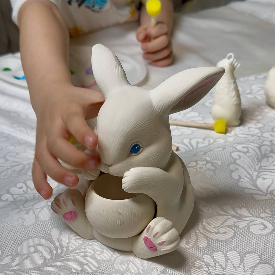 A child's hands decorating a custom Jesmonite bunny figurine during a kids candle making kit and painting activity, perfect for Easter craft kits for kids.