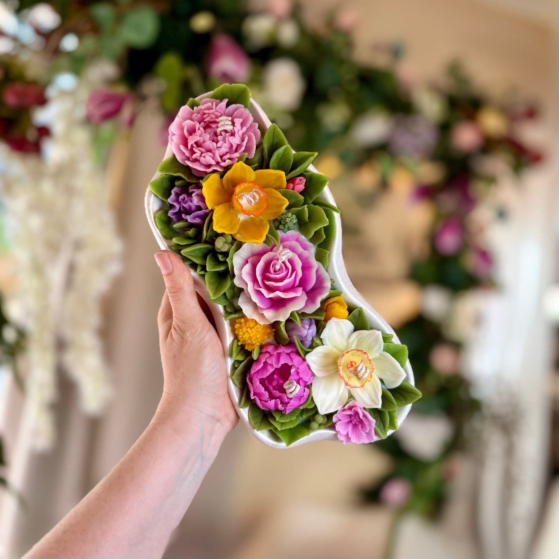 Showing the scale of the large 1.65kg floral candle held in hands against a garden backdrop.