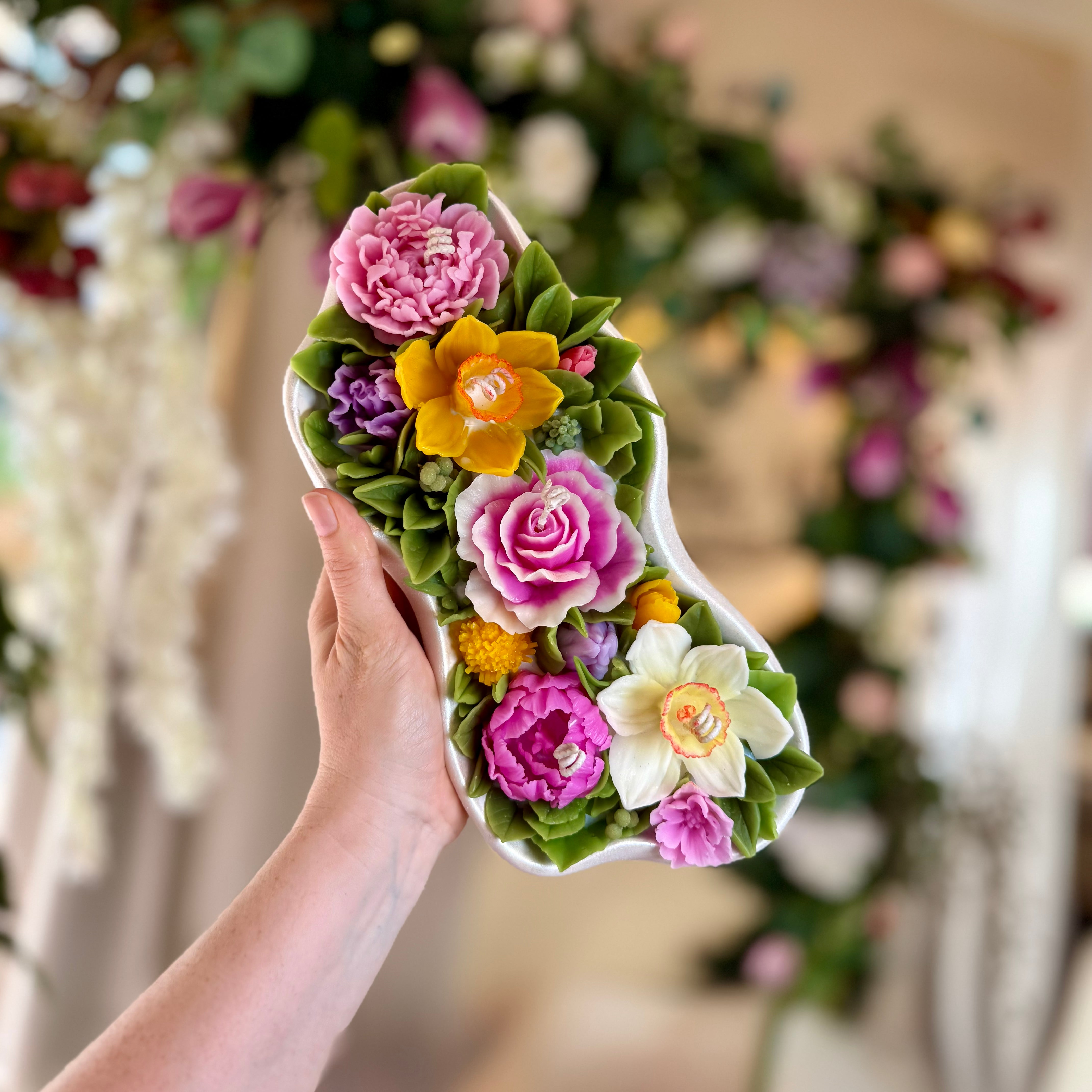 Showing the scale of the large 1.65kg floral candle held in hands against a garden backdrop.