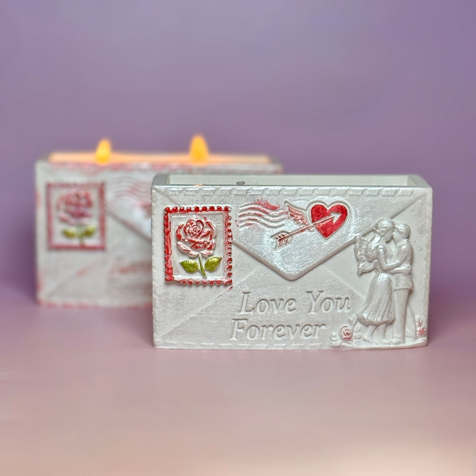 A pearl-white Jesmonite envelope candle holder with the inscription Love You Forever, a hand-painted red rose stamp, and a lit double-wick soy candle burning in the background.