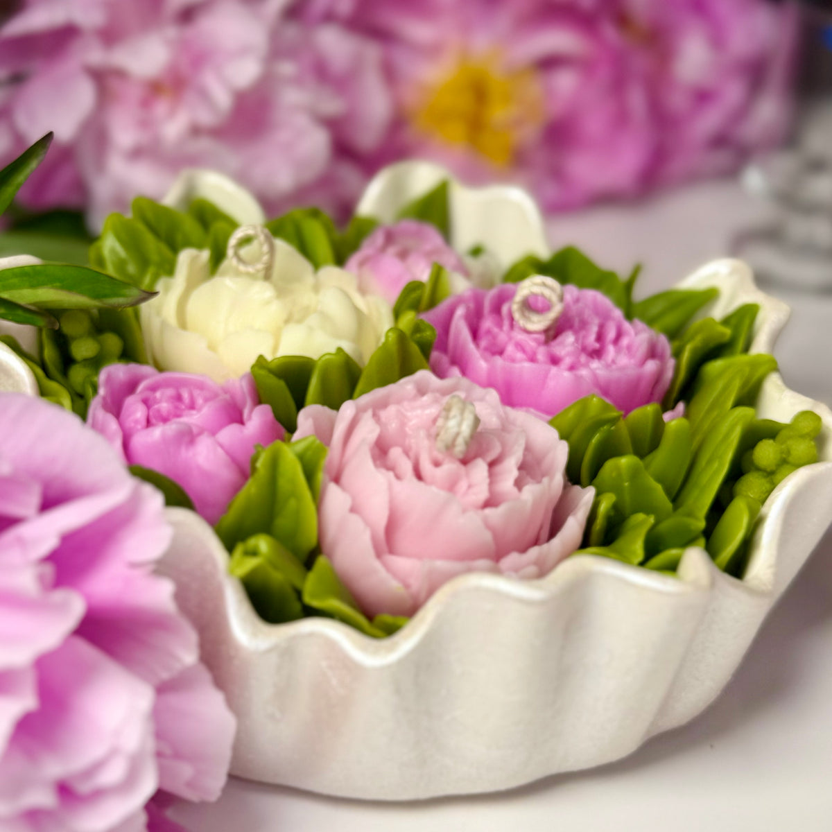 A close-up side view of a luxury Sarah Bernhardt peony multi-wick candle with decorative coiled cotton wicks, showcasing detailed pink and cream wax blossoms in a handcrafted pearl white Jesmonite scalloped bowl.