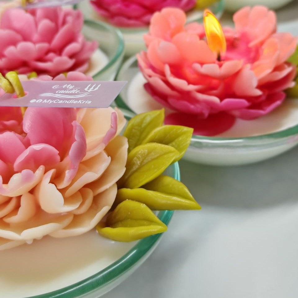 Burning sculptural peony candle with a glowing flame, featuring a hand-moulded beeswax flower.