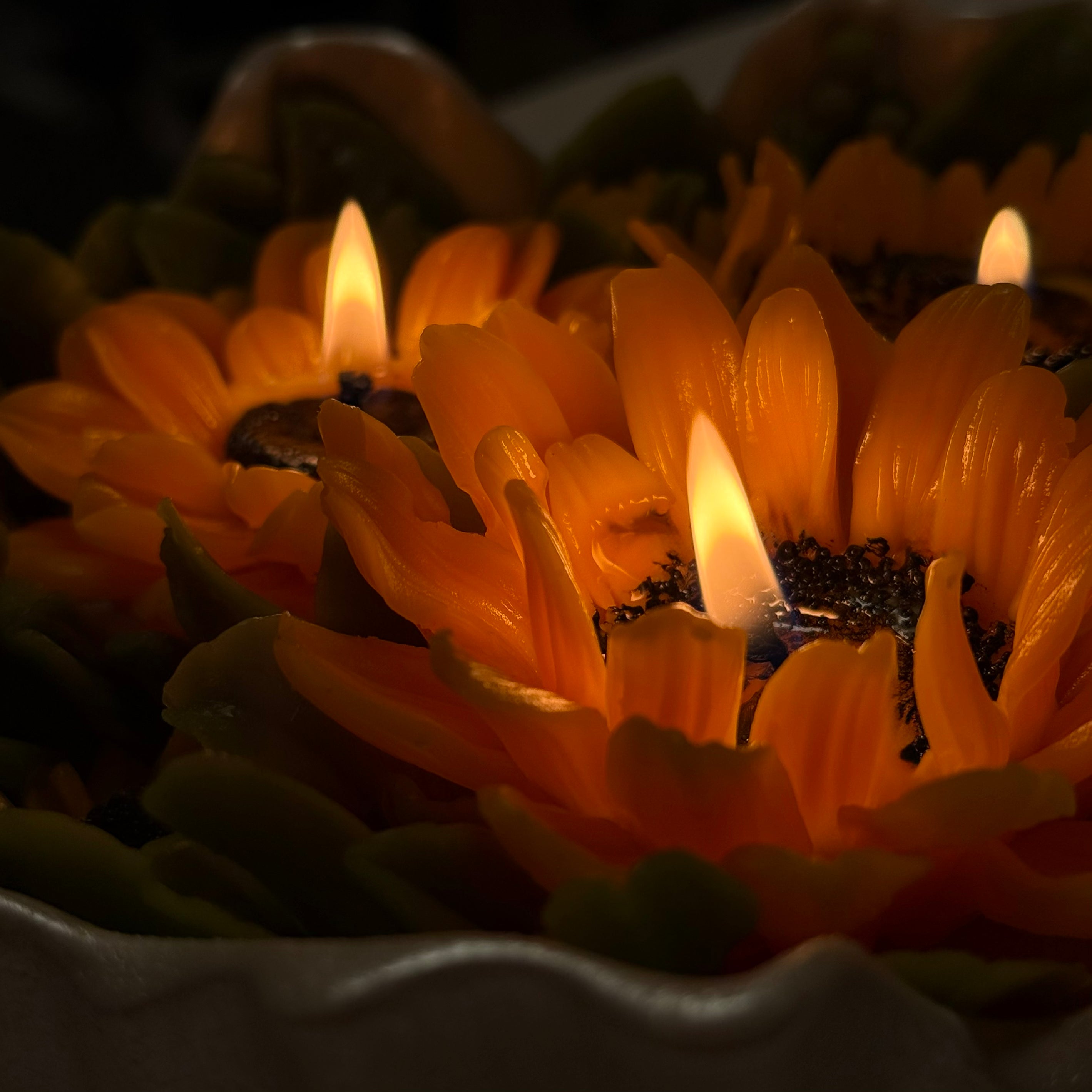 Extreme close-up of a luxury sunflower candle showing the warm glowing flame and detailed texture of hand-poured golden beeswax petals.