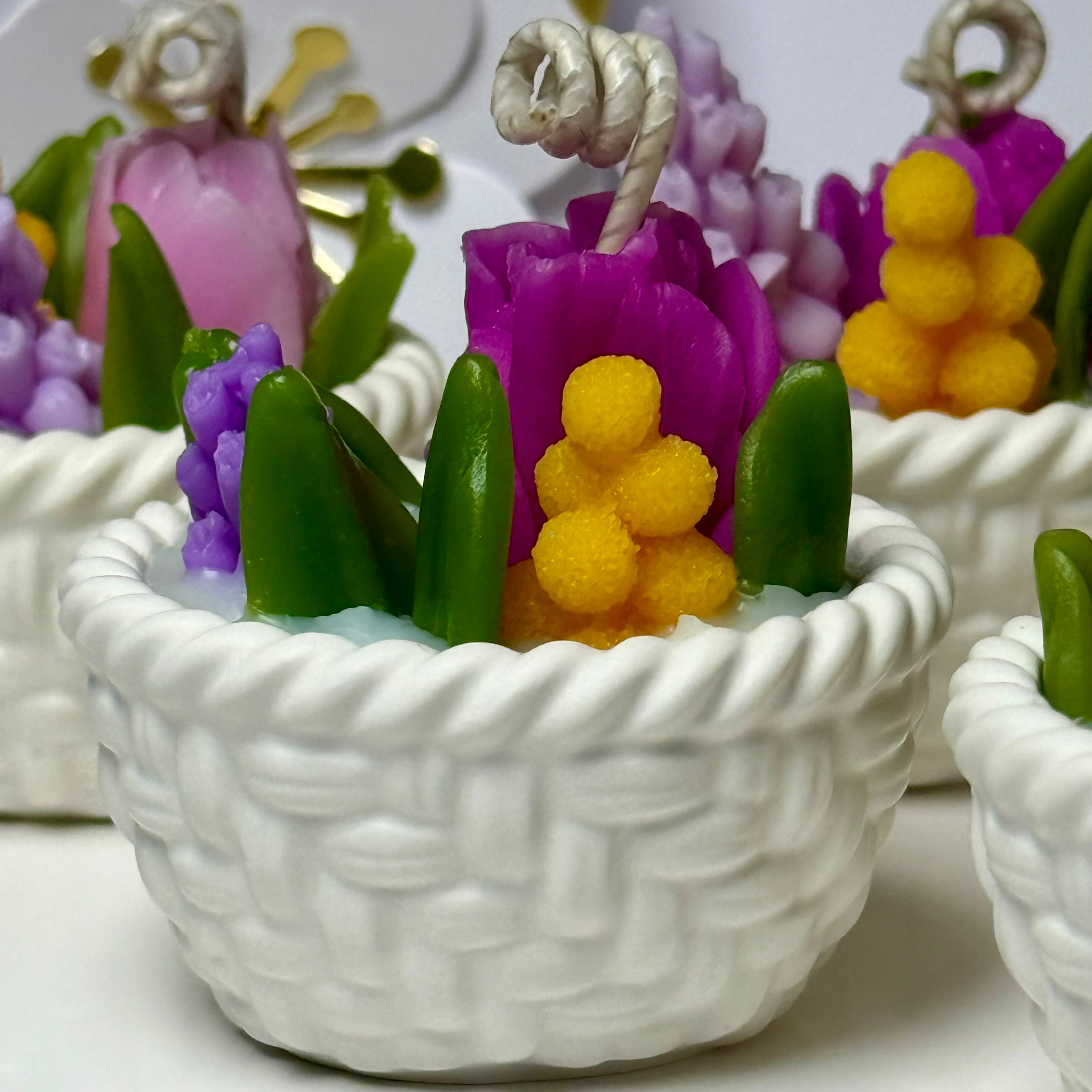 A macro close-up focusing on the vibrant purple and yellow hand-sculpted beeswax flower petals and green leaves arranged inside the white hand-cast Jesmonite woven basket.