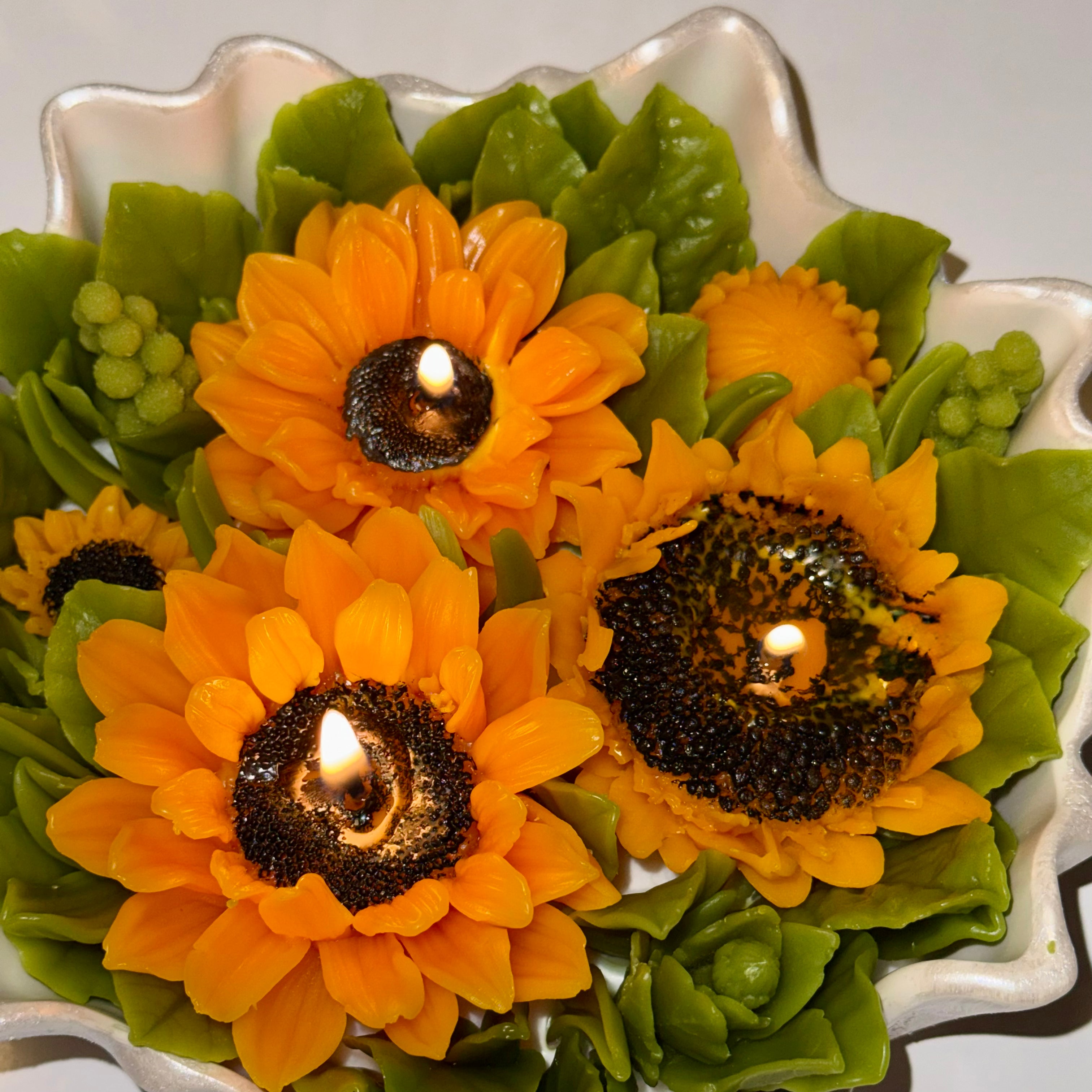 Top view of a newly lit sunflower multi-wick flower arrangement candle, illustrating the even placement of three burning wicks amidst yellow petals and green leaves.
