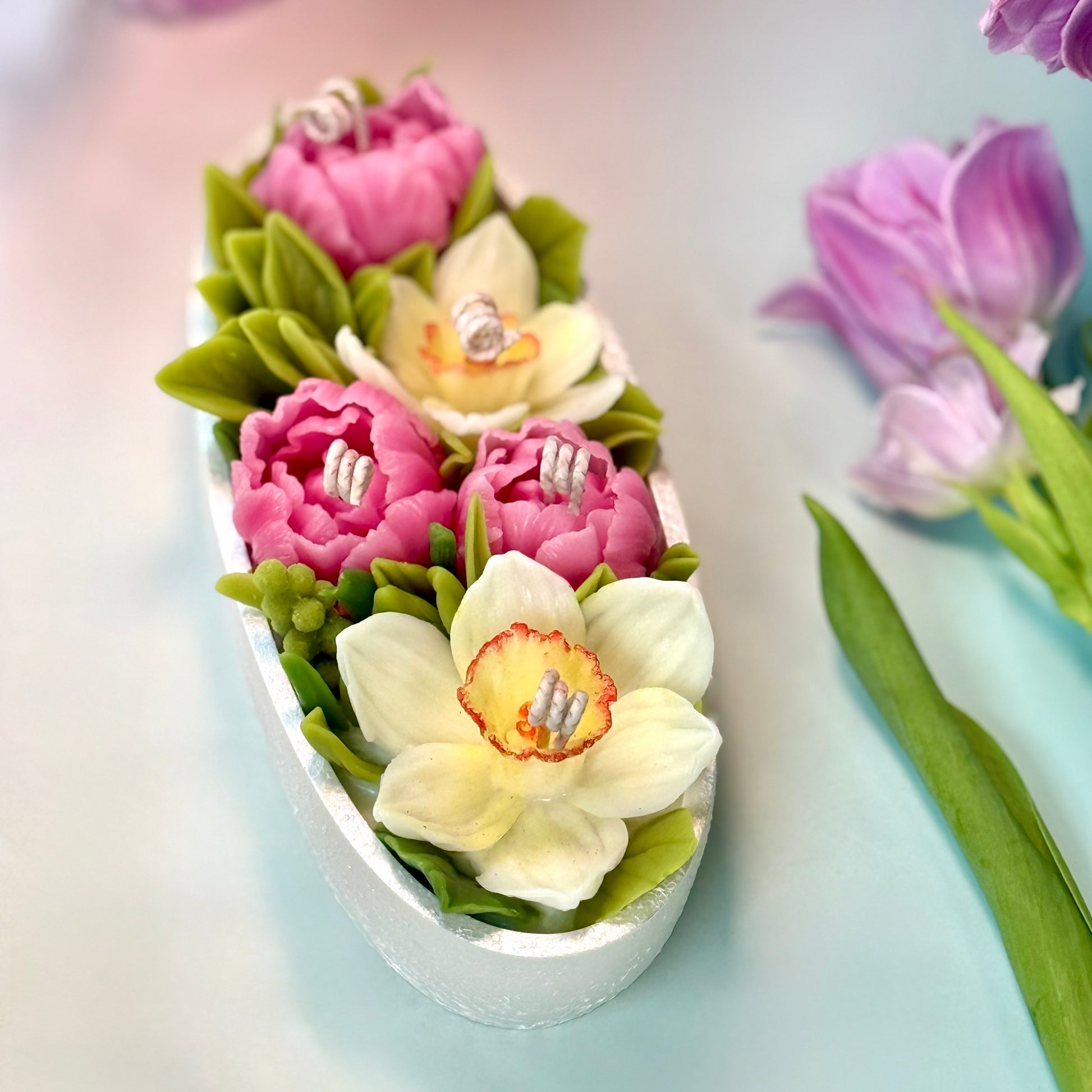 Top-down perspective of an oval artisan flower candle set with vibrant yellow daffodils and pink beeswax peonies, perfect as a luxury table centrepiece with gift box.