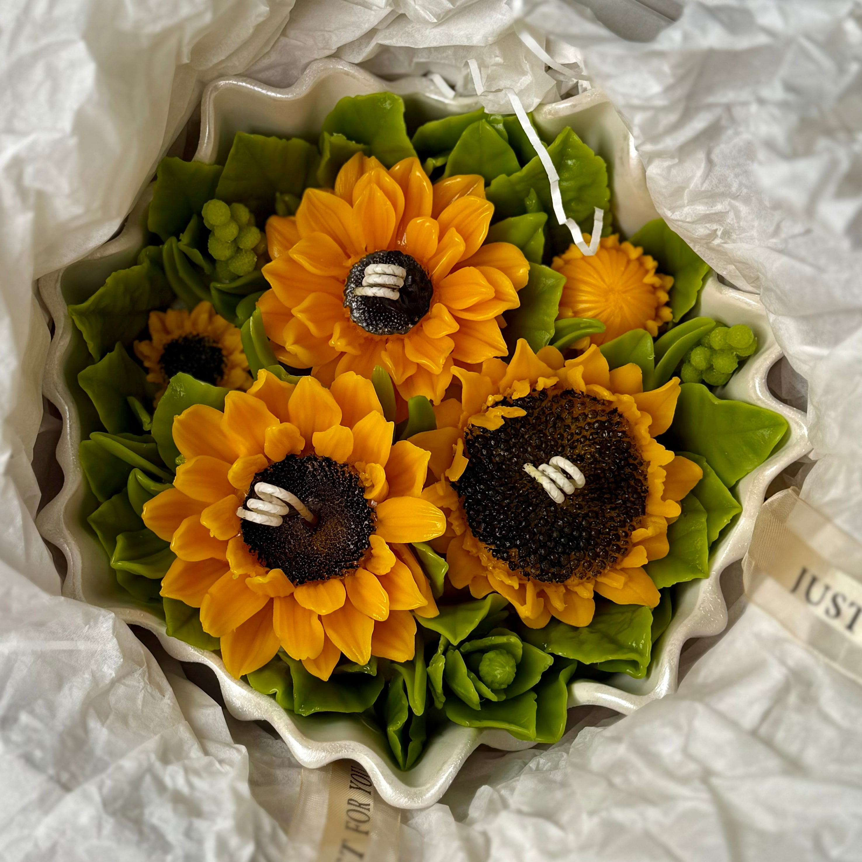Overhead view of the large sunflower bouquet candle nestled in white gift tissue paper inside its premium presentation box with a satin ribbon.
