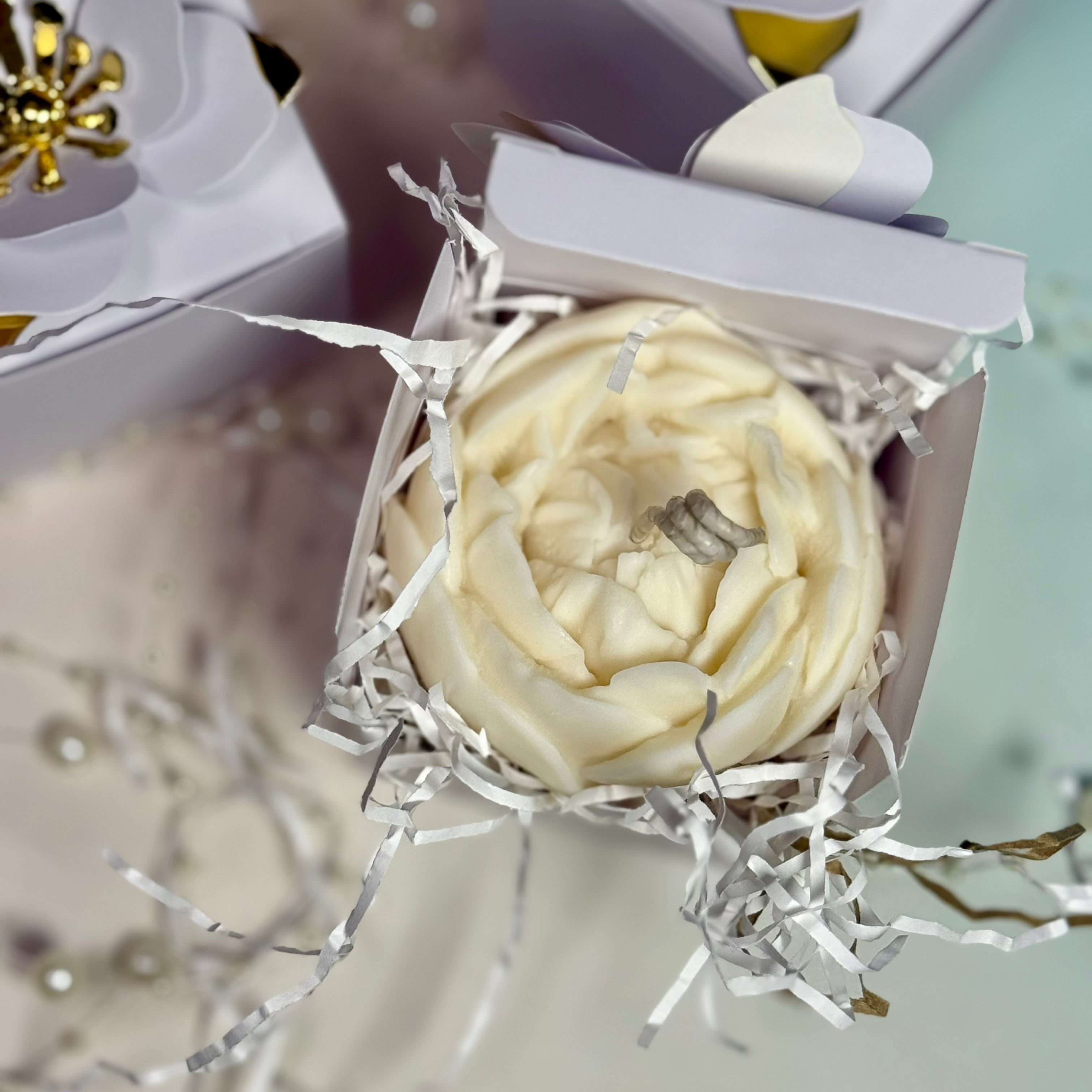 Looking down into a boutique white favour box protecting a detailed, ruffling soy wax peony flower candle ready to be given as a premium wedding guest token.