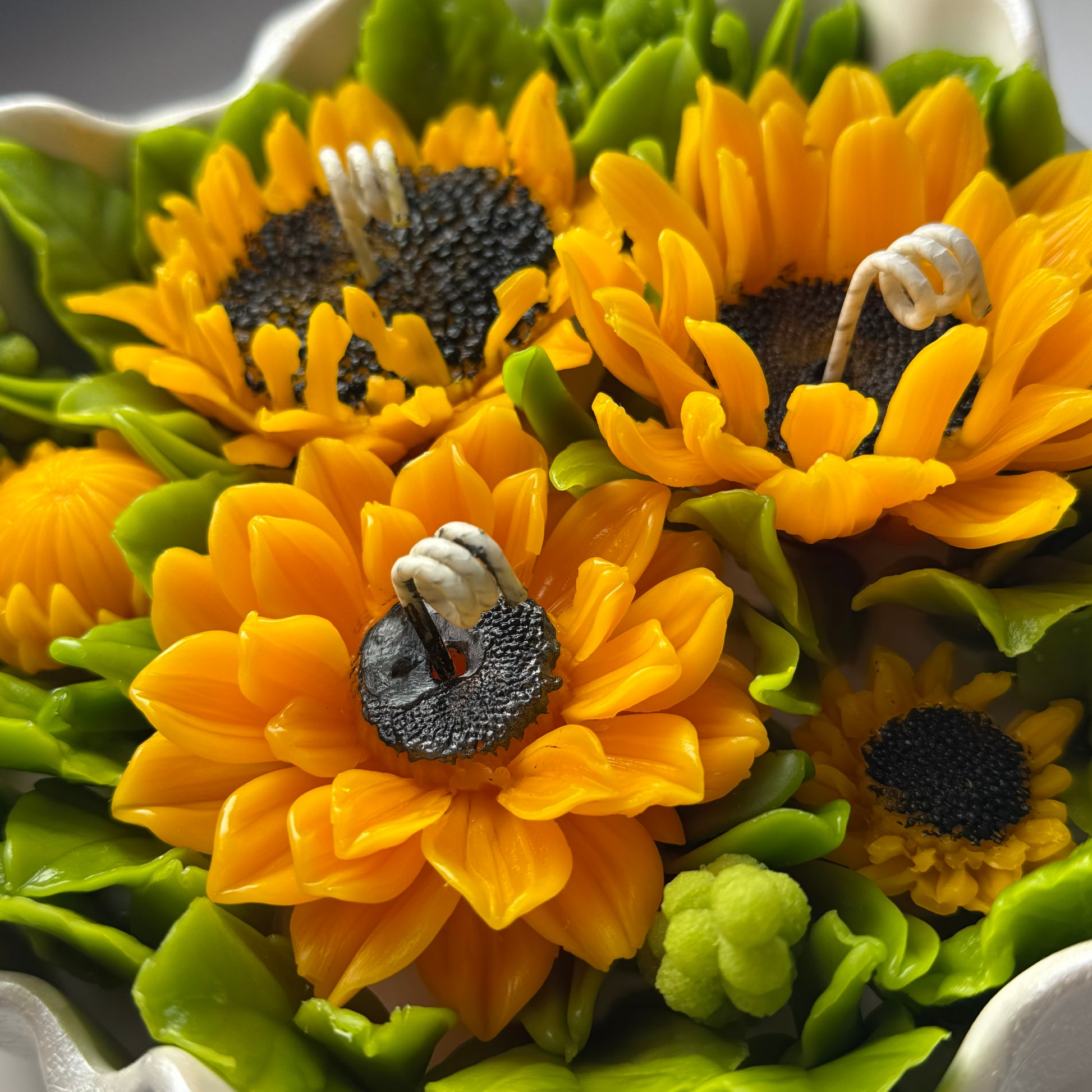 Detailed close-up macro shot of three realistic sunflower candle heads made of pure beeswax with textured black seed centres and small green berry accents.