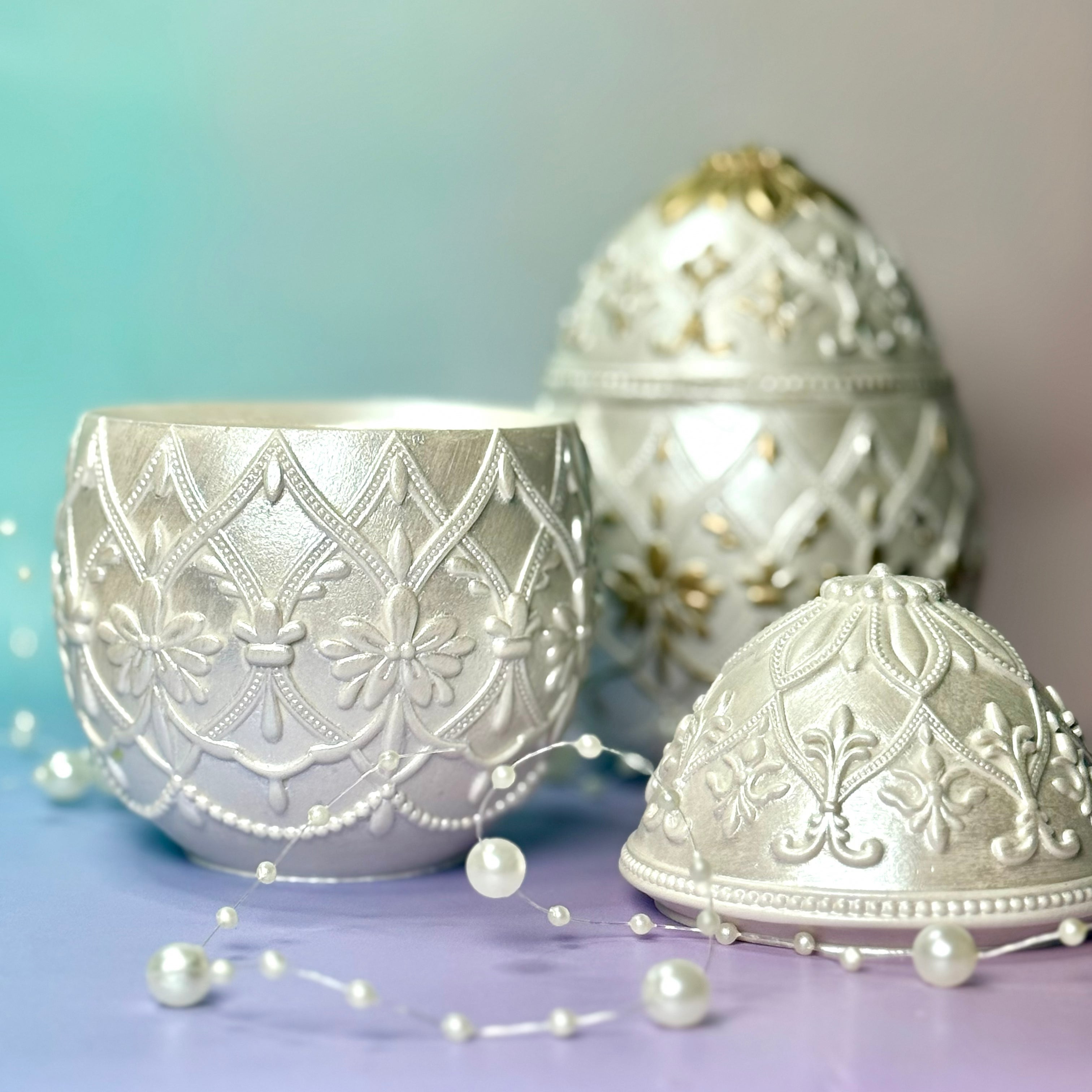 An open classic white Jesmonite Easter egg candle container showing the inside wax, with its decorative lid resting beside it, and a gold egg candle in the background.