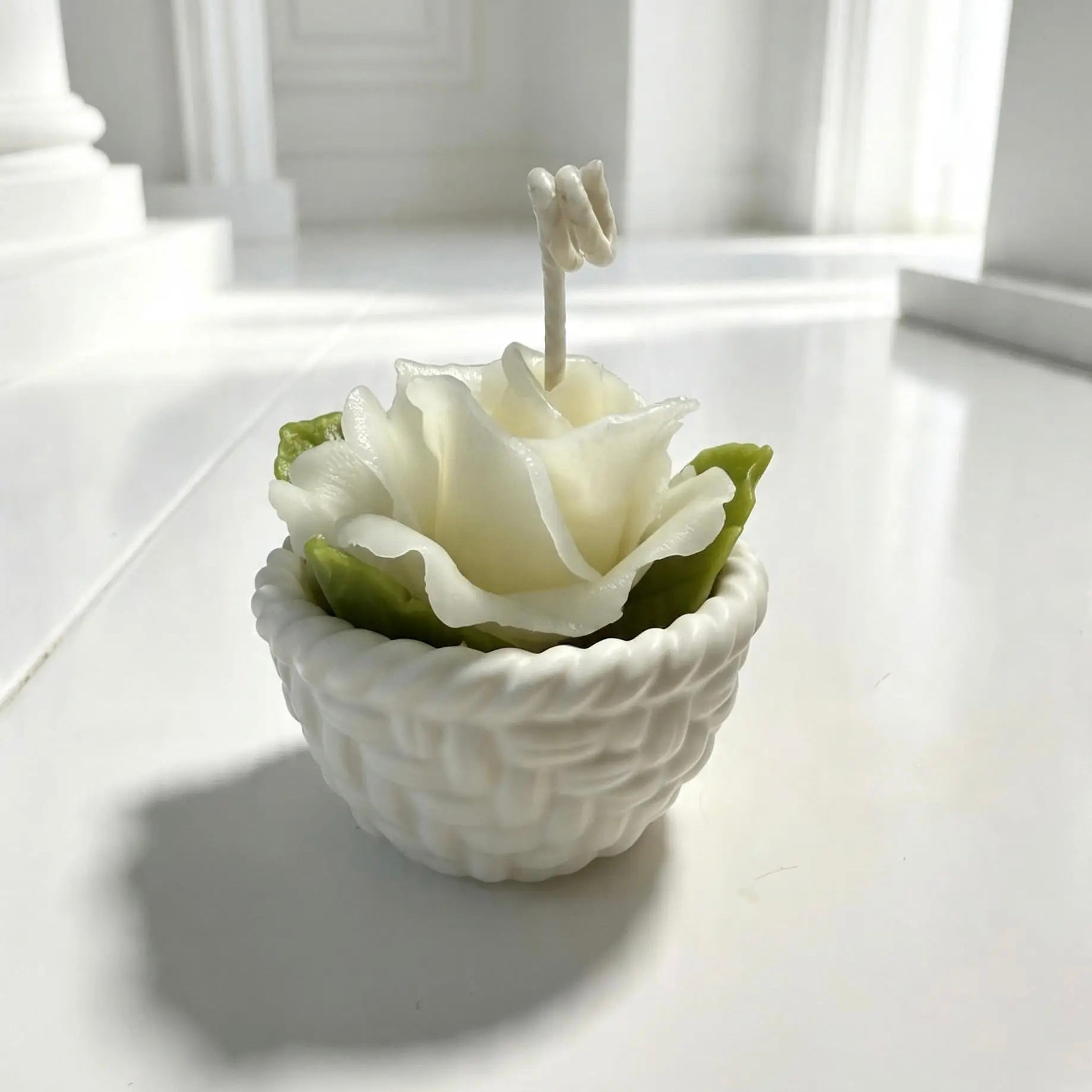 Handcrafted ivory rose candle with green leaves in a white Jesmonite woven basket pot.