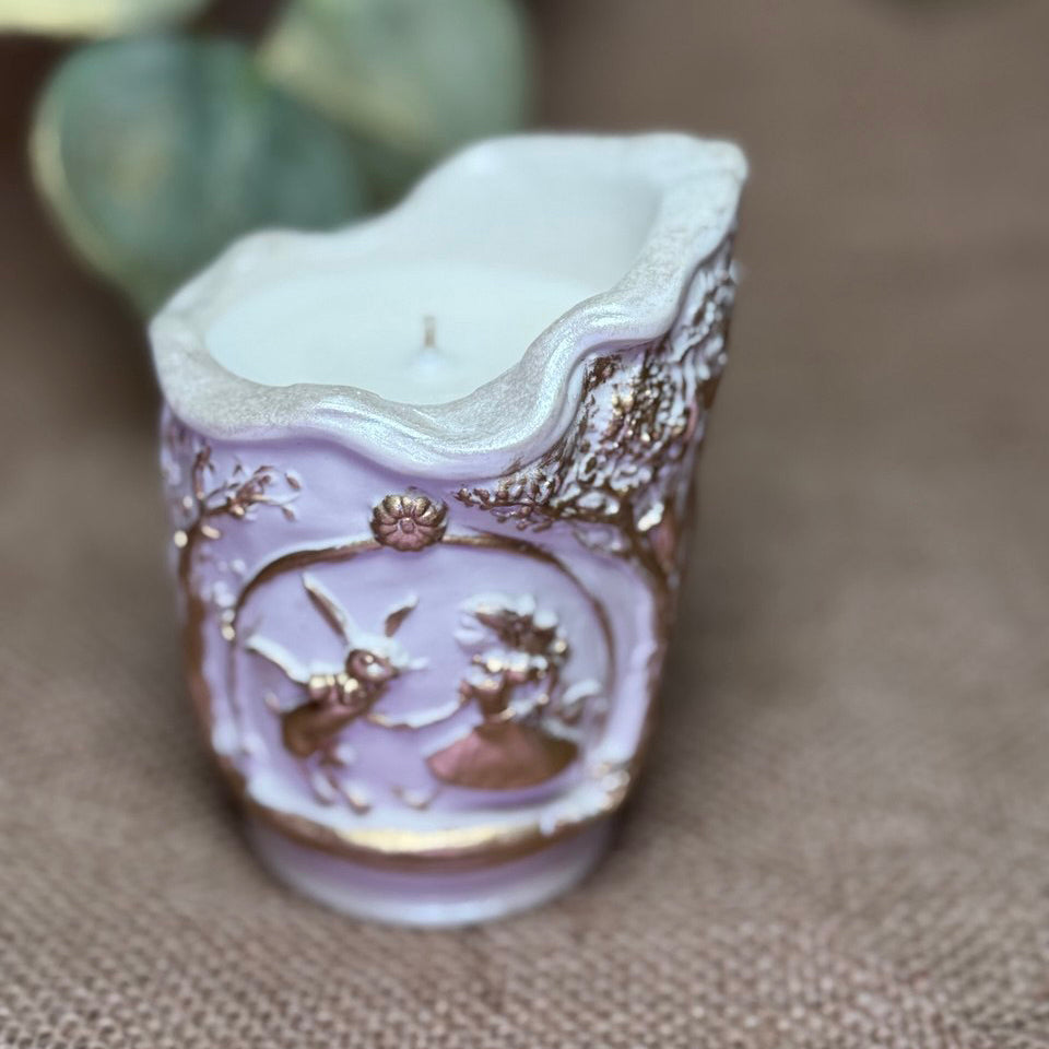 Slightly high-angle close-up of the scenic soy candle, showing the hand-poured natural wax and single cotton wick inside the ornate pearl-white and liquid gold container