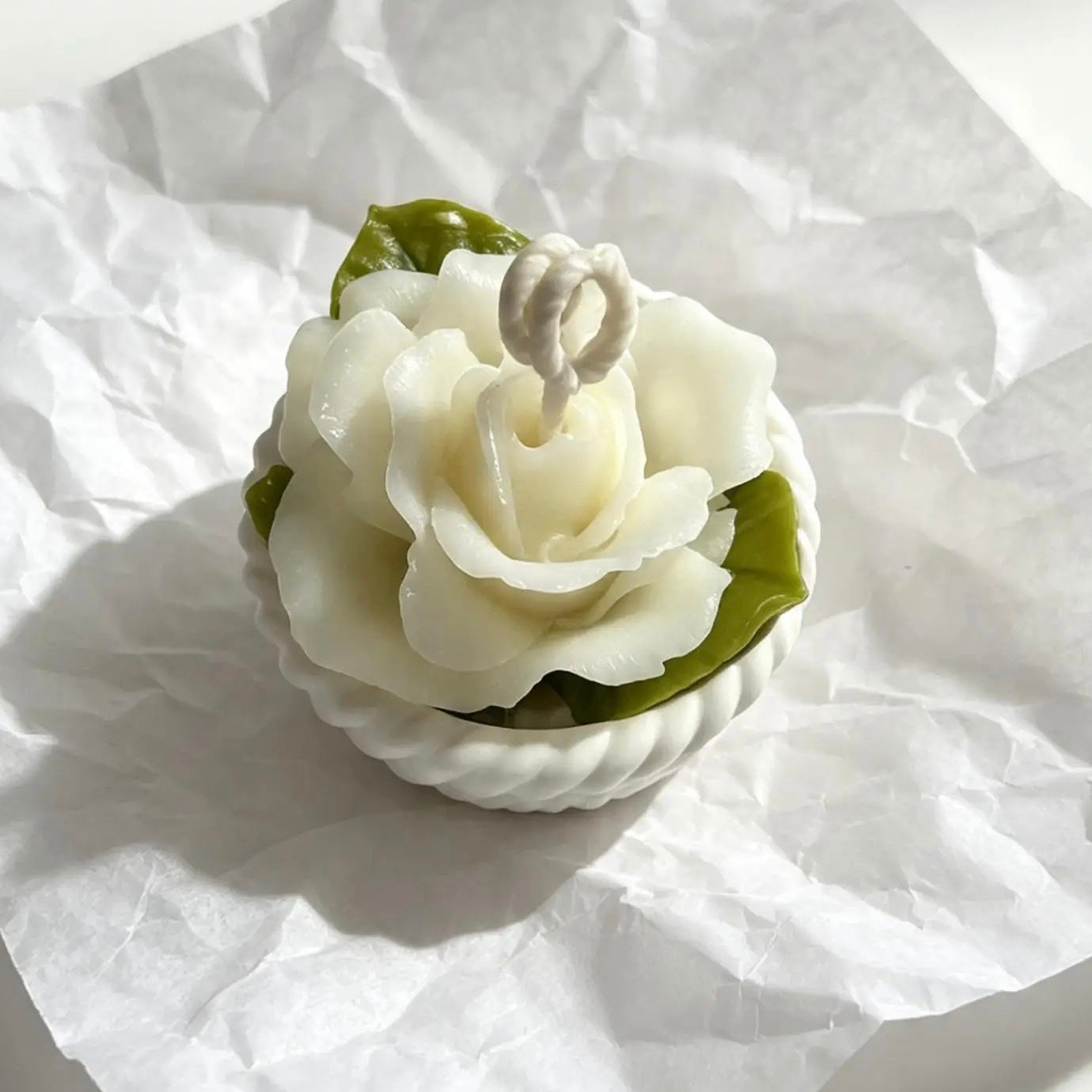Top view of a hand-sculpted white rose candle displaying detailed petals and green leaf accents.