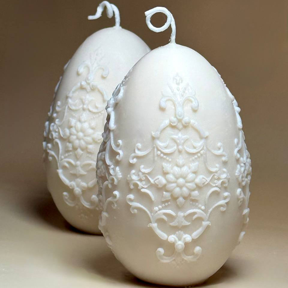 Two handmade sculptural Easter egg soy candles showing the intricate ornamental relief design from the front and side angles.