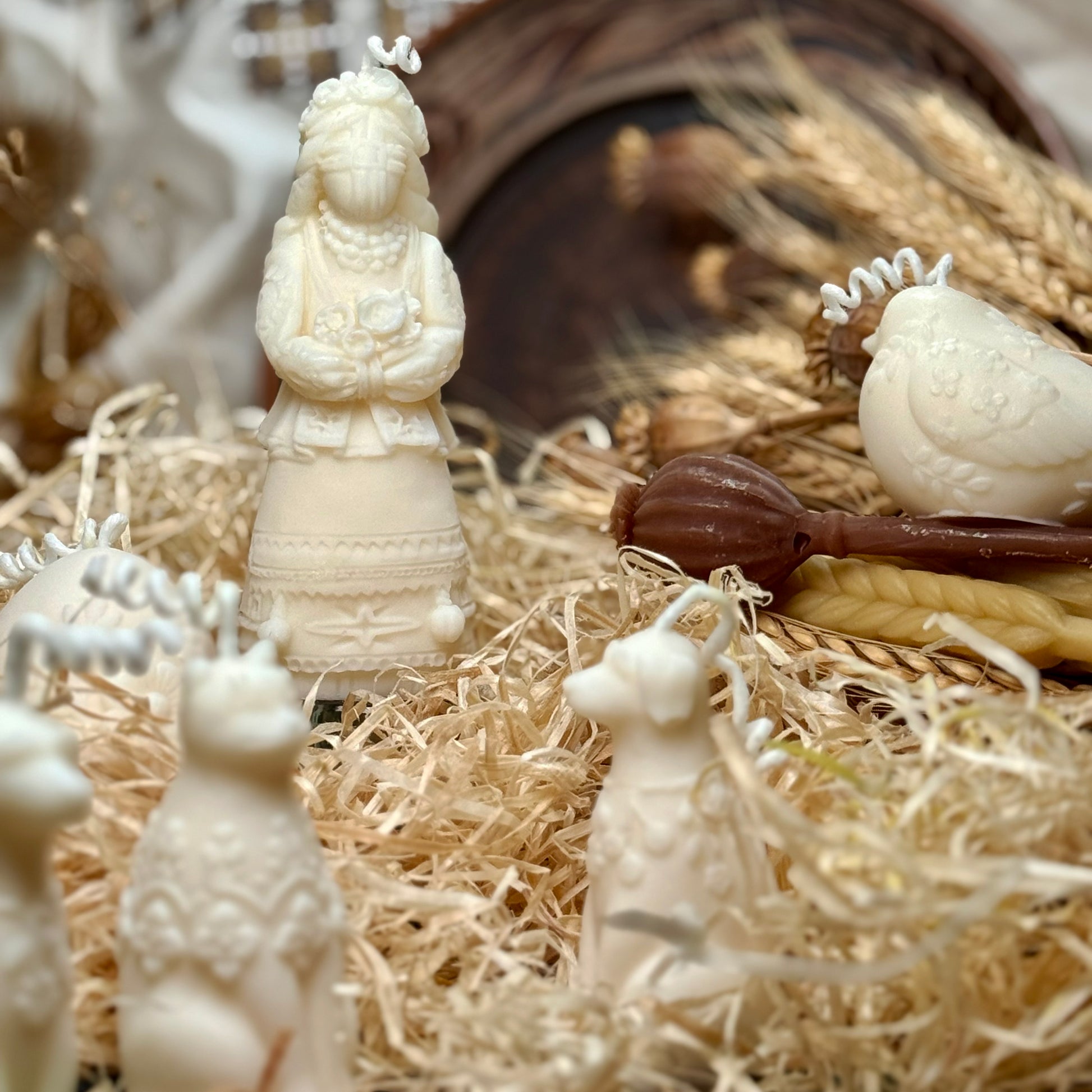 A front-facing view of the handcrafted Ukrainian Motanka talisman candle displayed on a rustic wooden log slice, showcasing the prominent symbolic cross pattern on the doll's face.