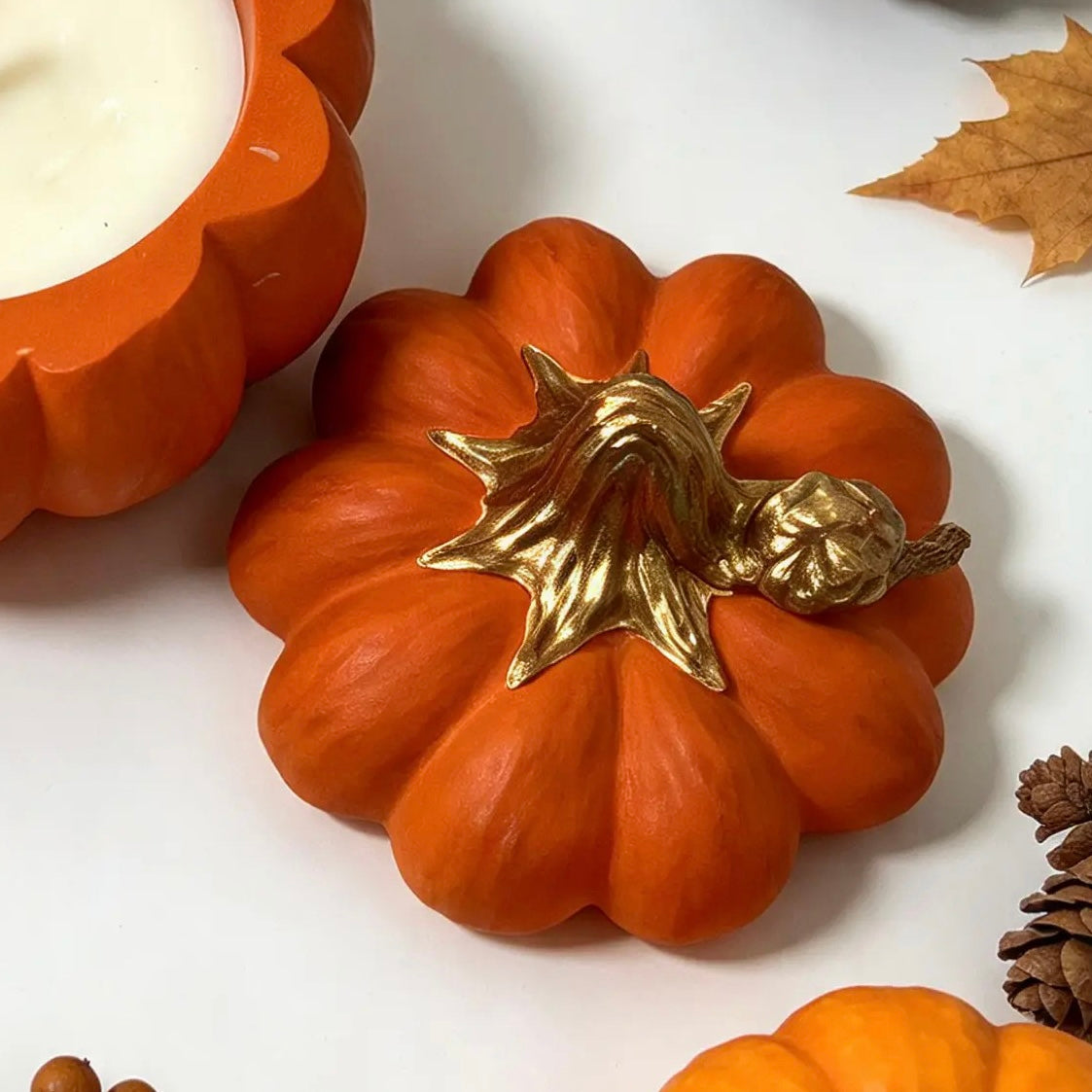 Top view of smooth orange Jesmonite pumpkin candle lid with hand-painted gold stem next to soy wax jar